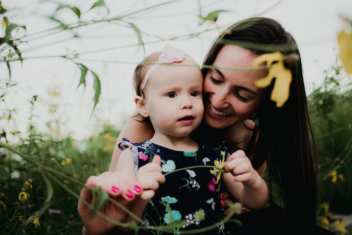 Sweet embrace between parent and toddler surrounded by yellow flowers in a garden.