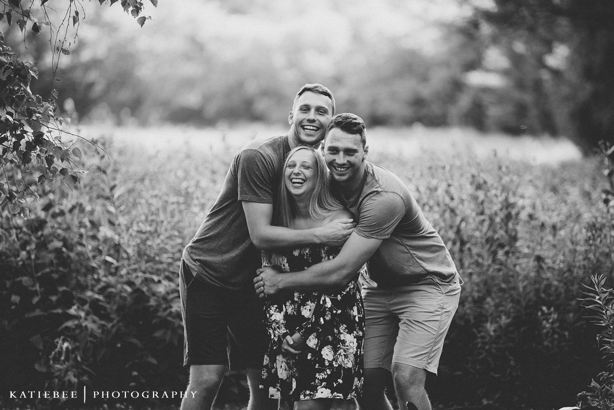 Black and white photo of three people embracing and laughing in a wildflower meadow.