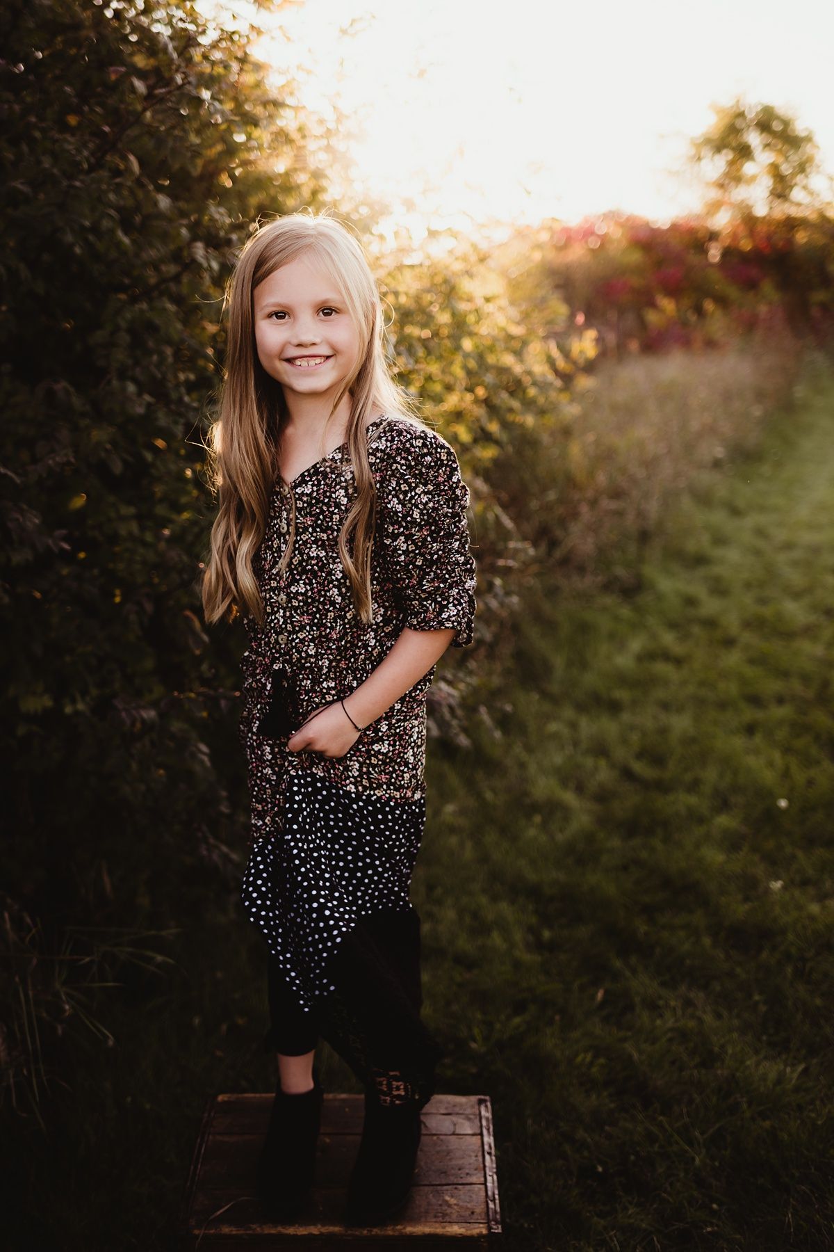 Young person in patterned dress poses on wooden platform during golden hour.