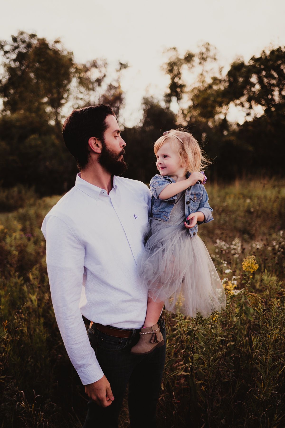 Parent holding child wearing tulle dress during golden hour outdoor photoshoot.