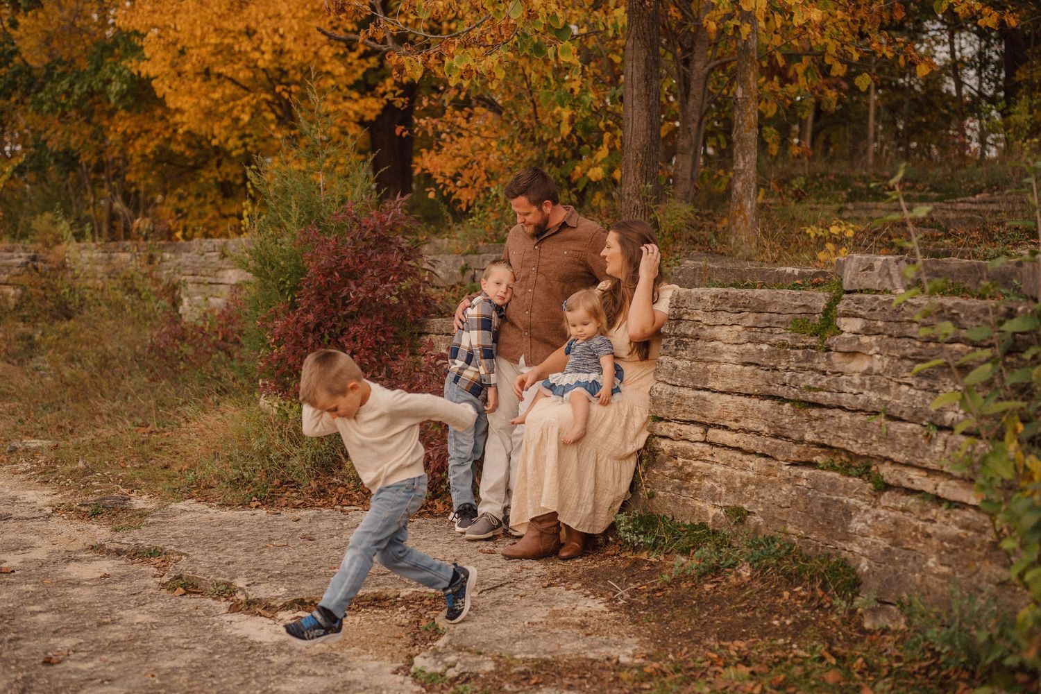Family enjoying a playful autumn photoshoot on rustic wooden steps surrounded by fall foliage.