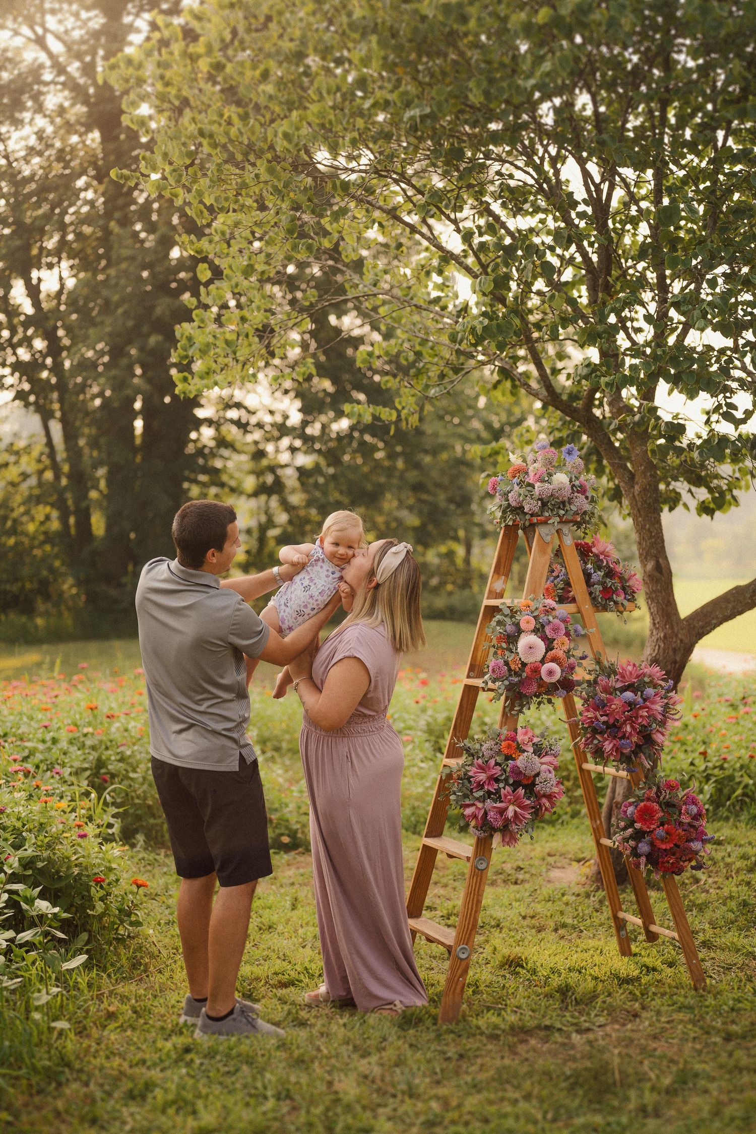 A romantic outdoor photo session in a sun-dappled garden with a wooden A-frame arch decorated with pink and purple flowers.