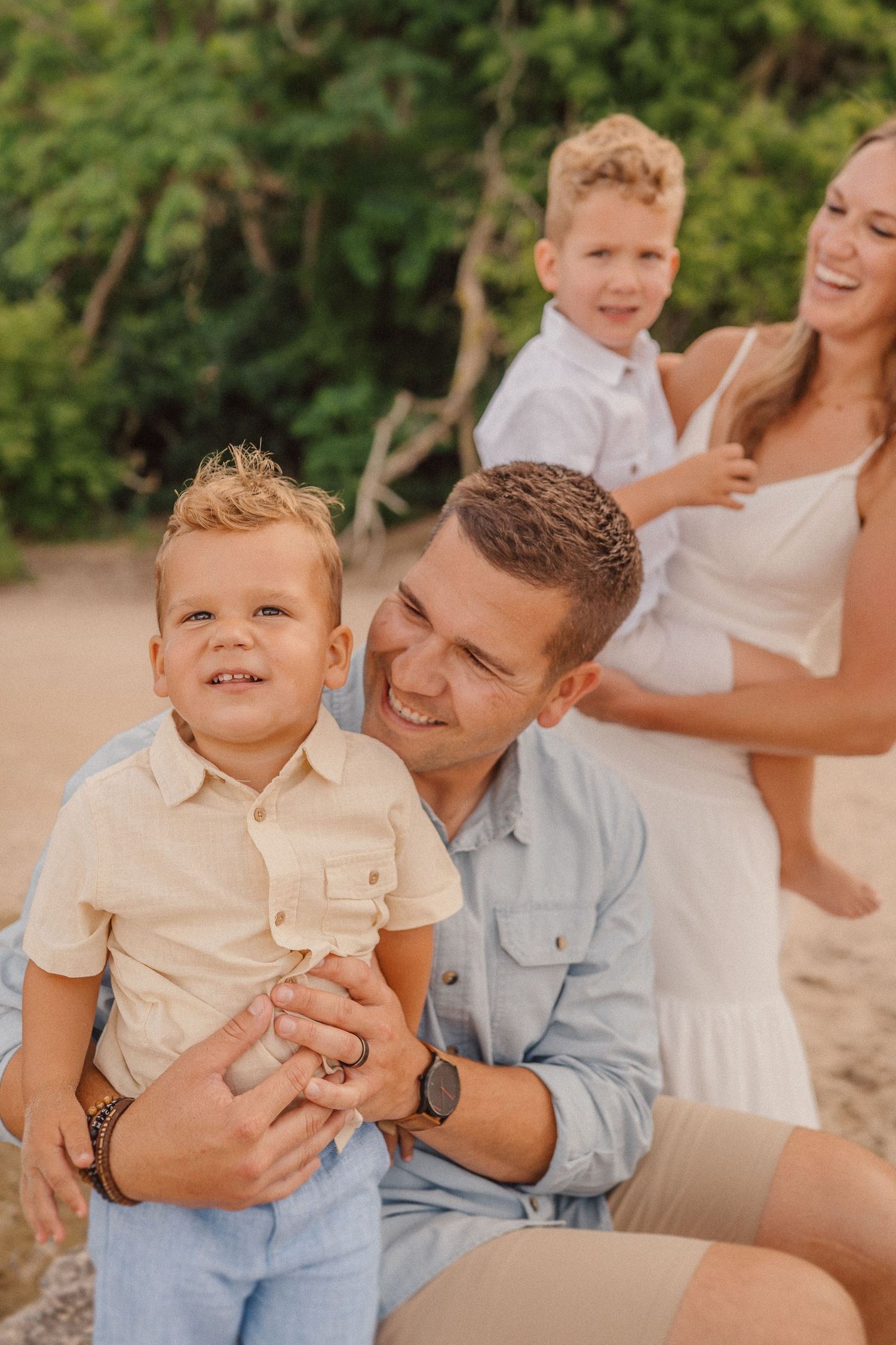 Candid family moment captured at sunset on a beach with natural greenery in background.