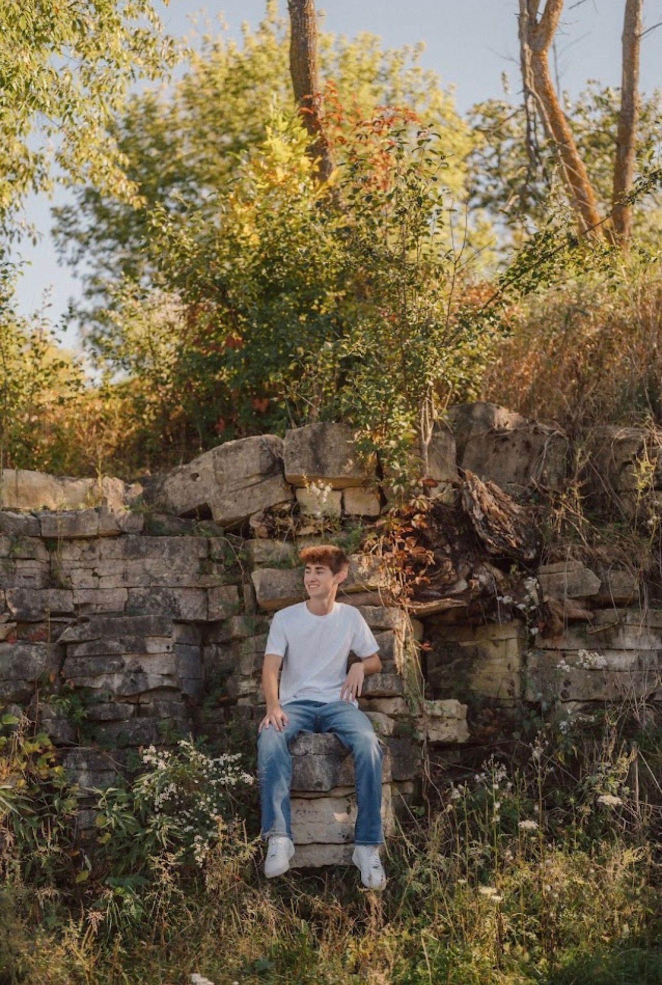 Casual portrait on rustic stone wall surrounded by autumn foliage.