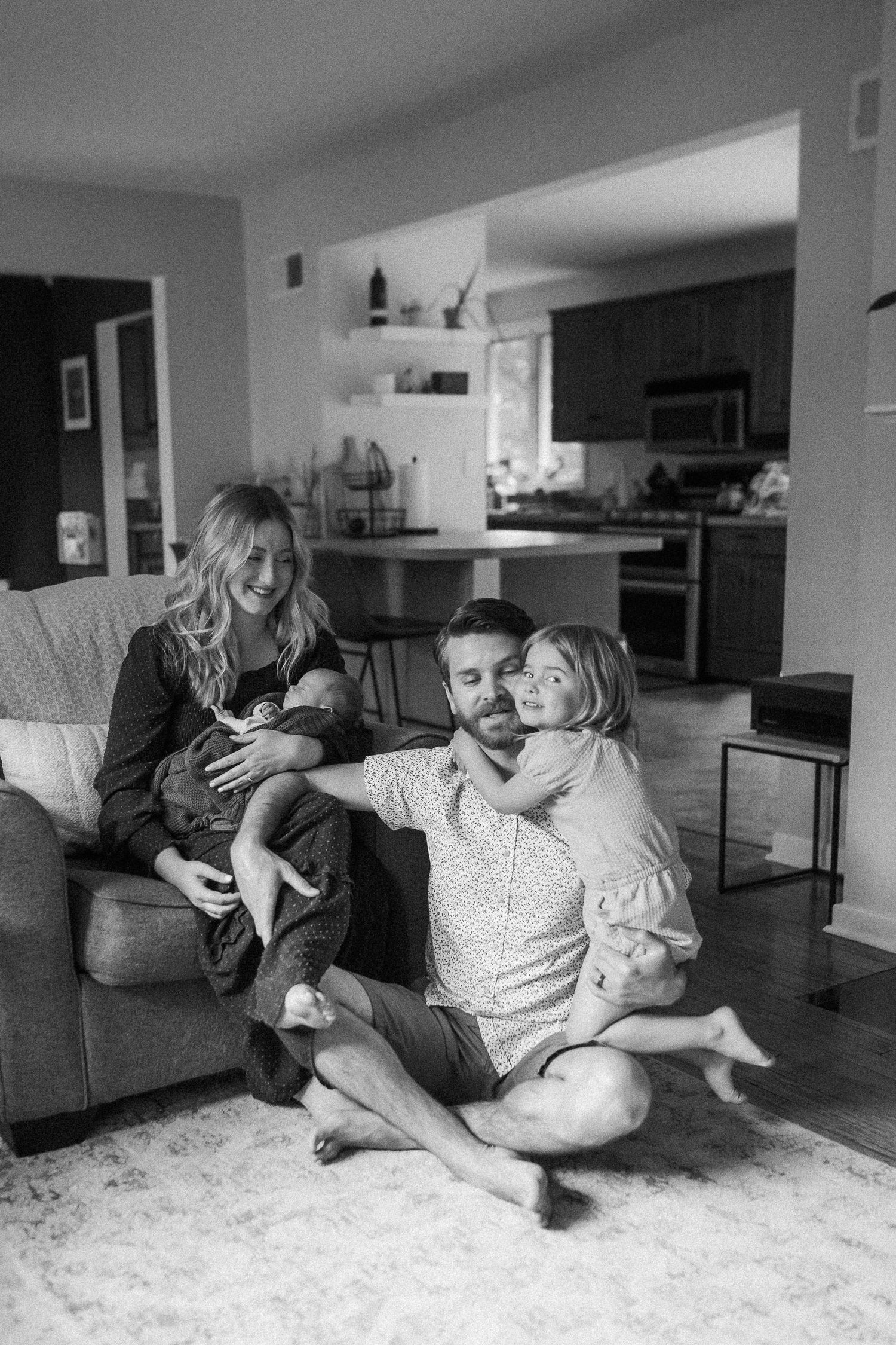 Black and white portrait of a family sharing an intimate moment on their living room couch.