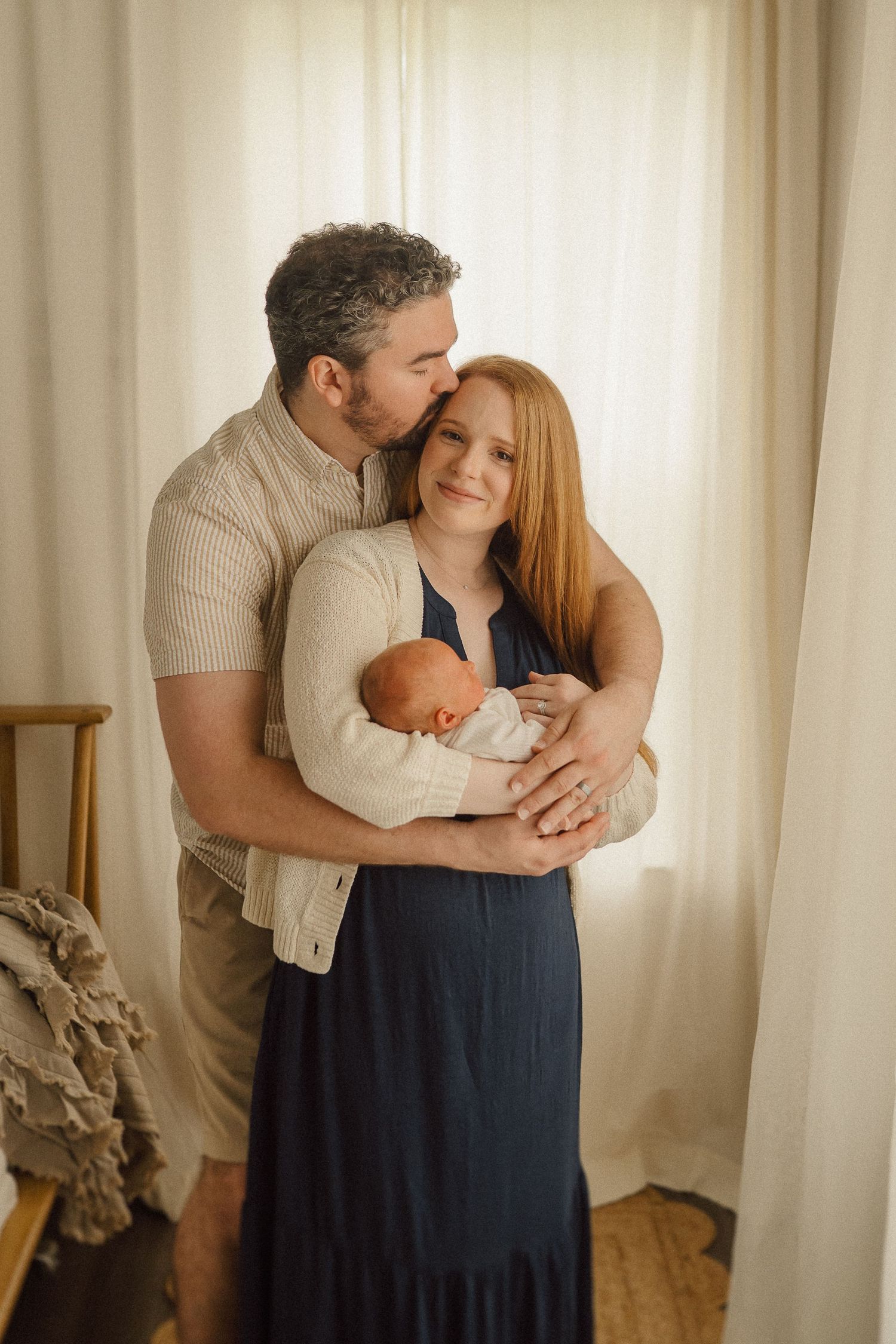 Intimate family portrait showing parents embracing while holding their newborn baby.