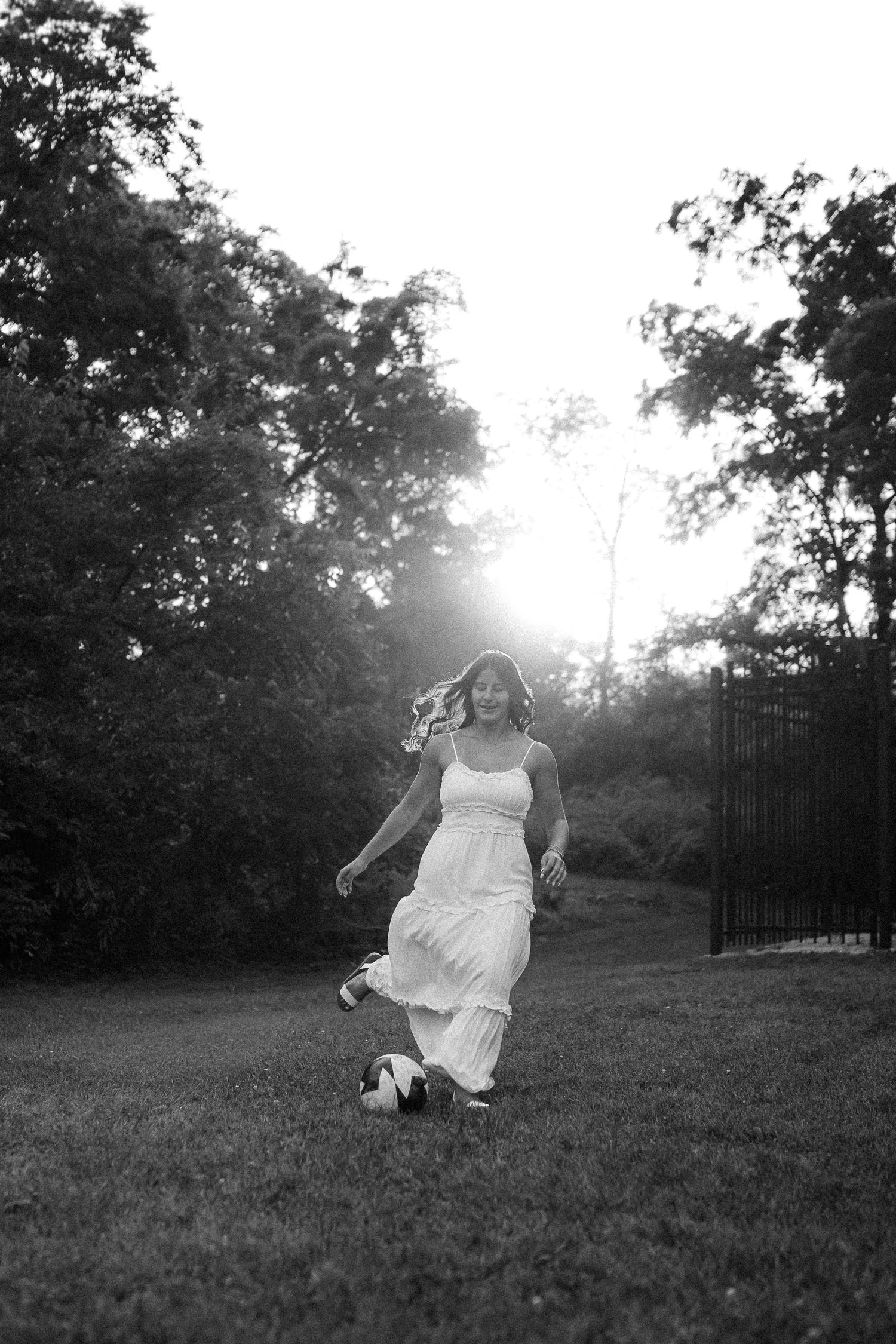 Black and white photo of a person in a white dress spinning in a grassy field at sunset.