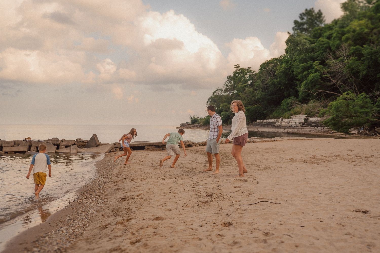 Beautiful coastal landscape with beach, trees, and clouds during golden hour as people walk along the shore.