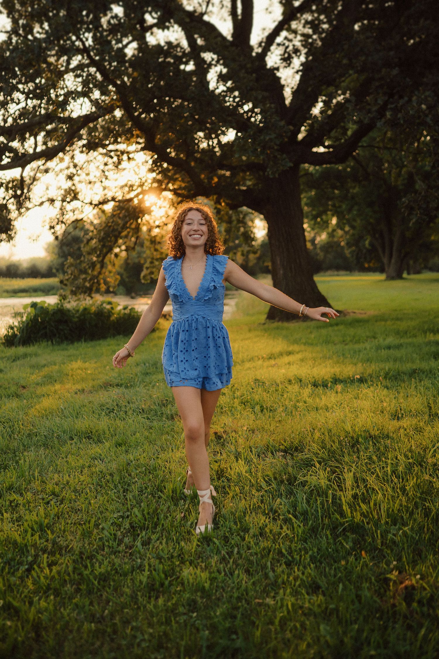 A carefree figure dances in a blue romper against the backdrop of a setting sun and towering trees.