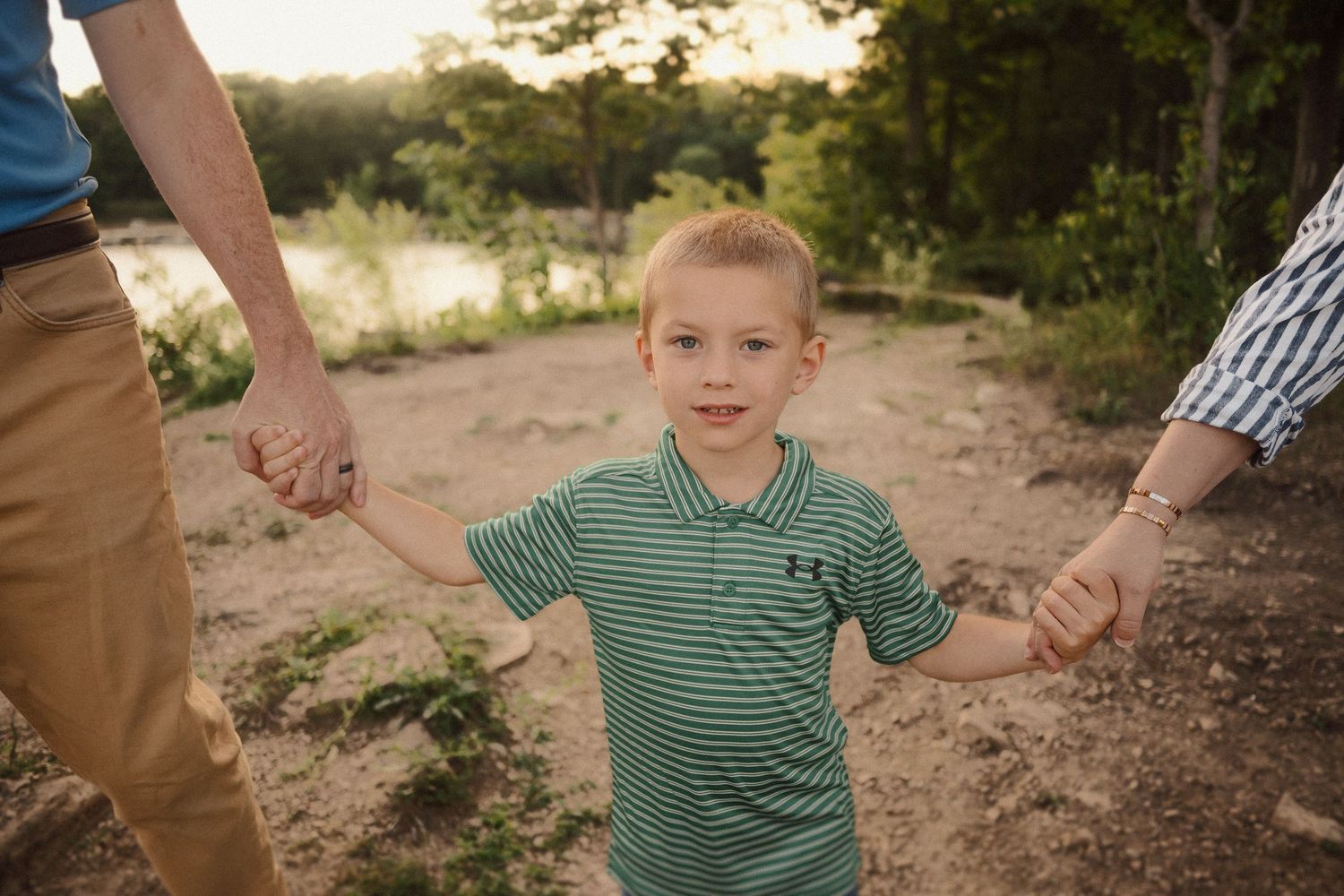 A happy child runs holding hands with adults in an outdoor setting at sunset.
