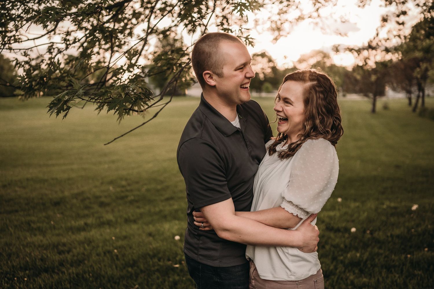 Couple laughing together in a sunny park setting during golden hour.