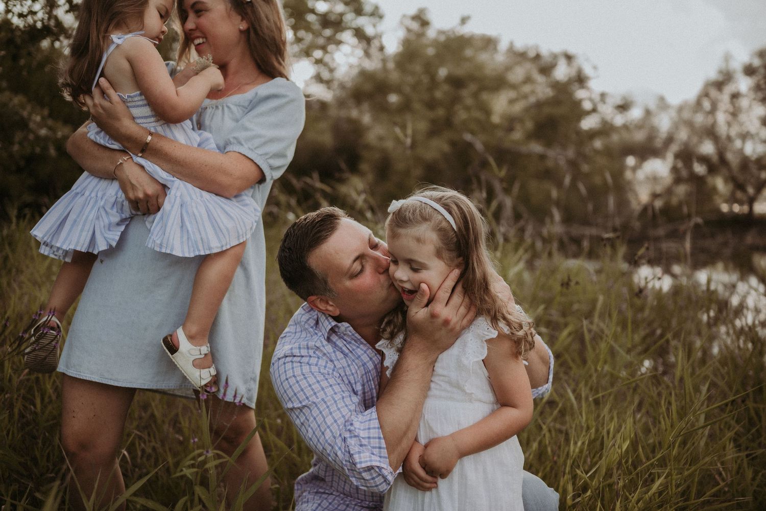 Family portrait in a field with adults and children sharing joyful moments together.