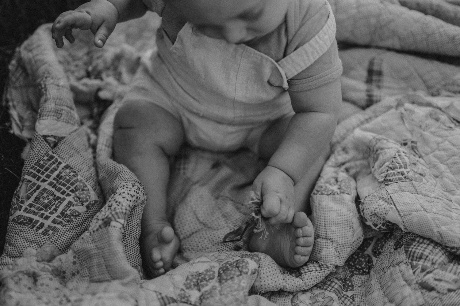 Black and white close-up of baby's feet on patterned blanket during outdoor session.