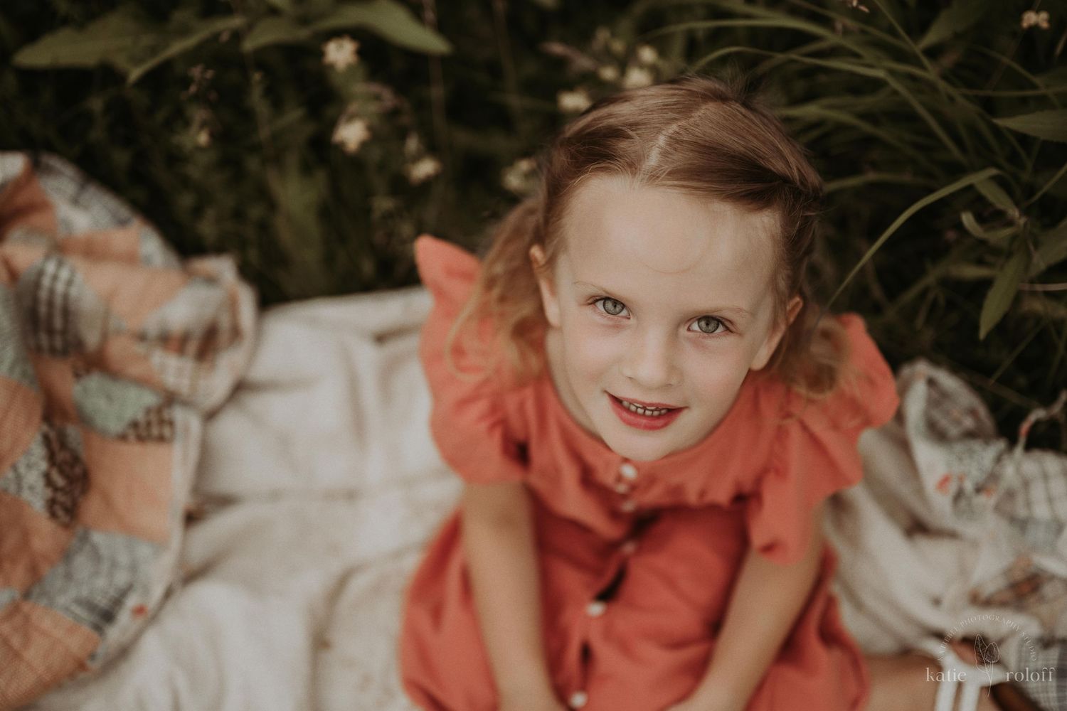 Child in coral dress sitting on blanket outdoors.