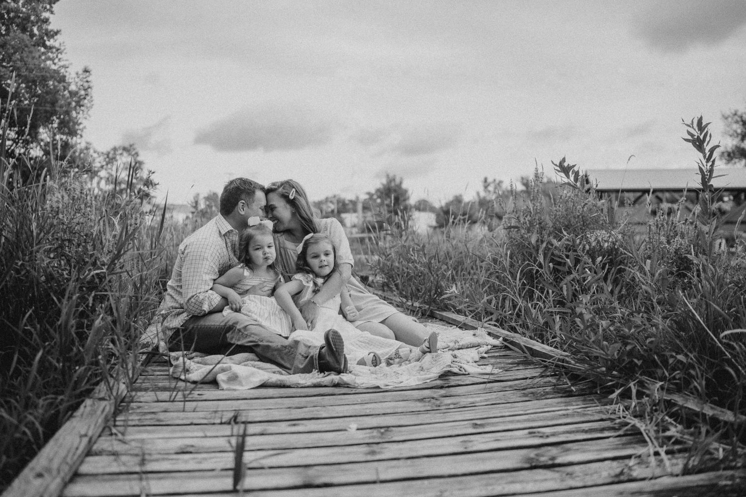 Group sitting together on a wooden boardwalk surrounded by tall grass on a cloudy day.
