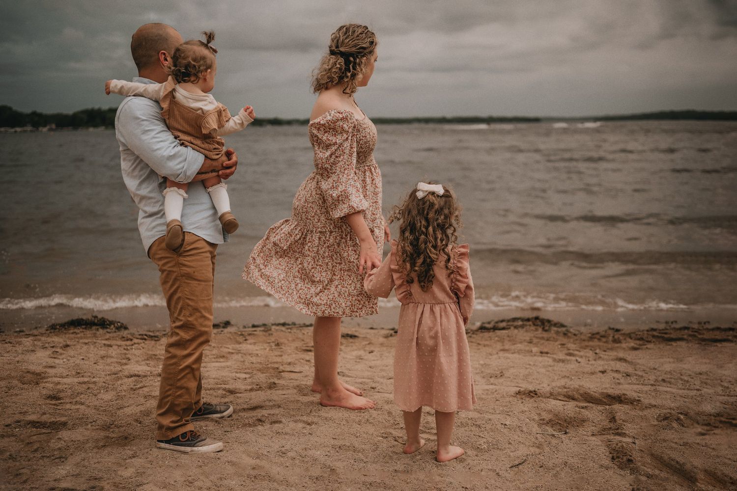 A warm family portrait against a moody beach backdrop during sunset.