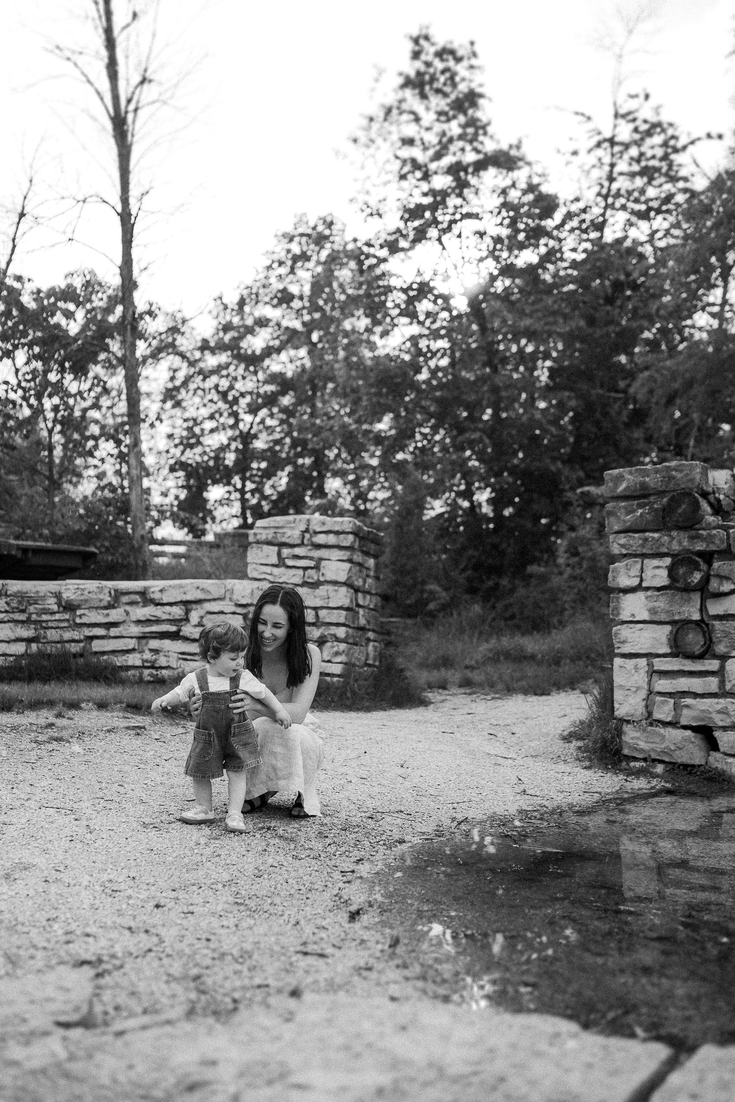 Black and white photo of a touching moment by stone pillars in a natural outdoor setting.