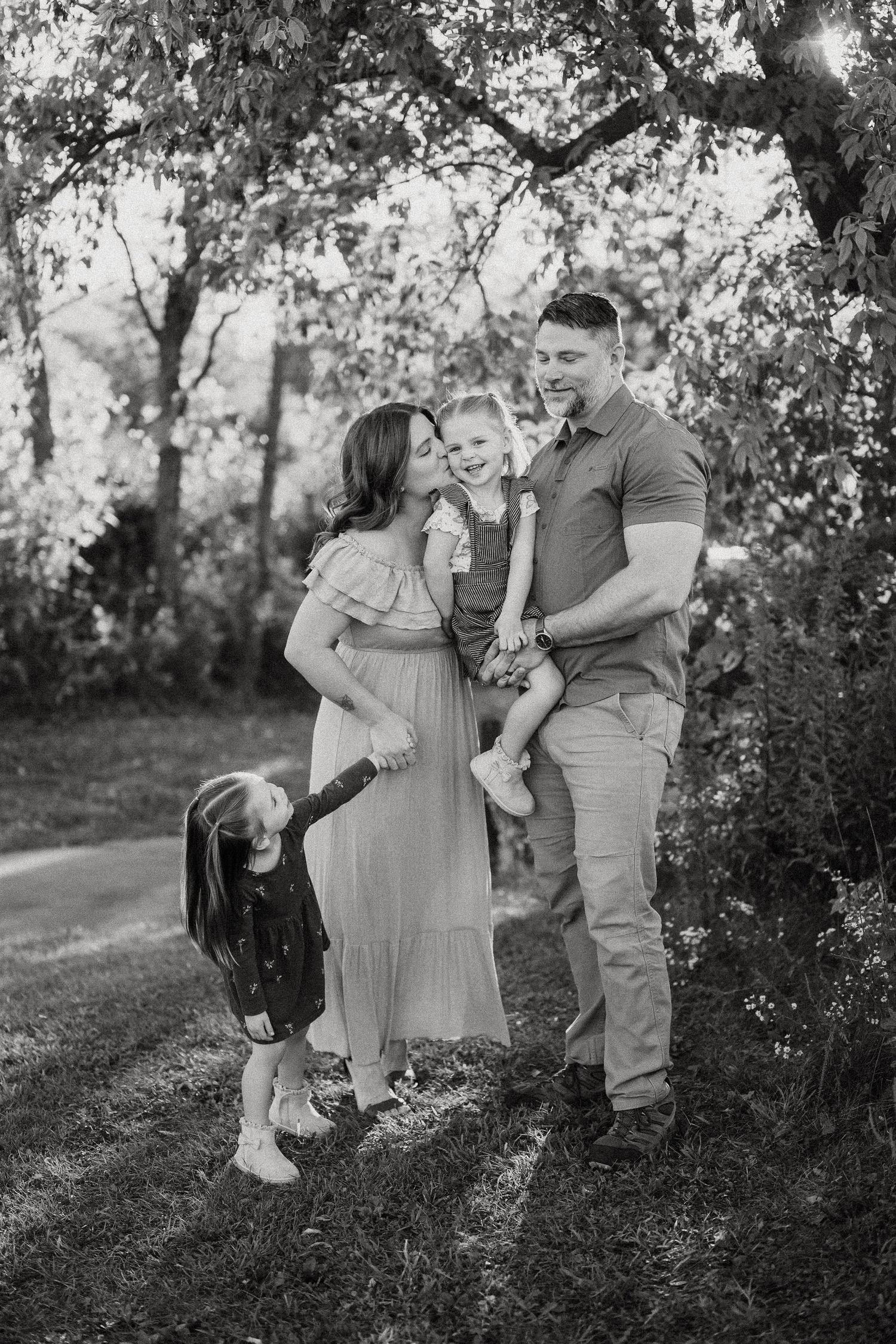 A playful family photoshoot in black and white showing candid moments outdoors among trees.