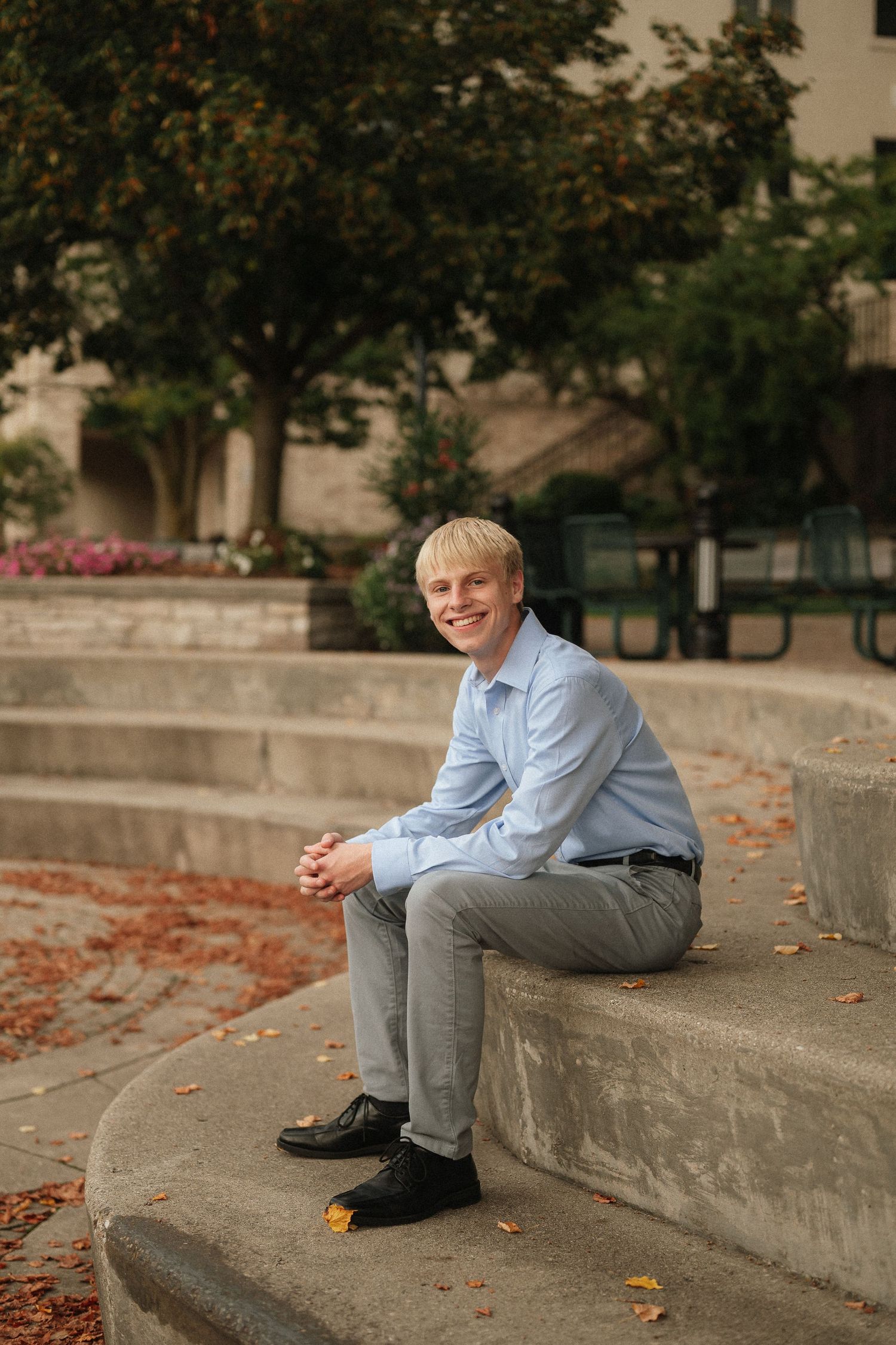 A casual outdoor portrait session showing someone relaxing on concrete steps with autumn leaves scattered around.