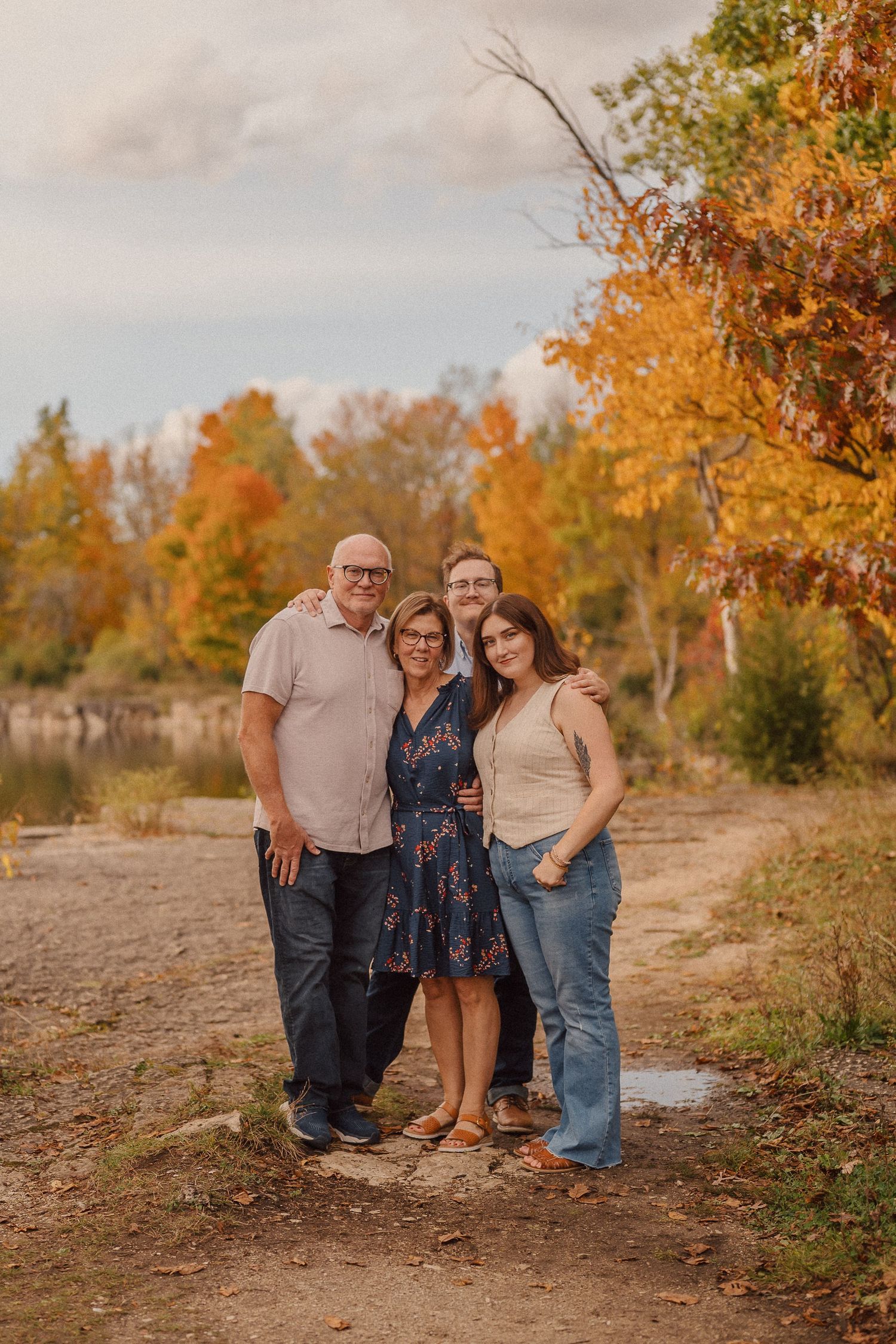 A casual outdoor family portrait captured against a backdrop of fall foliage and natural terrain.