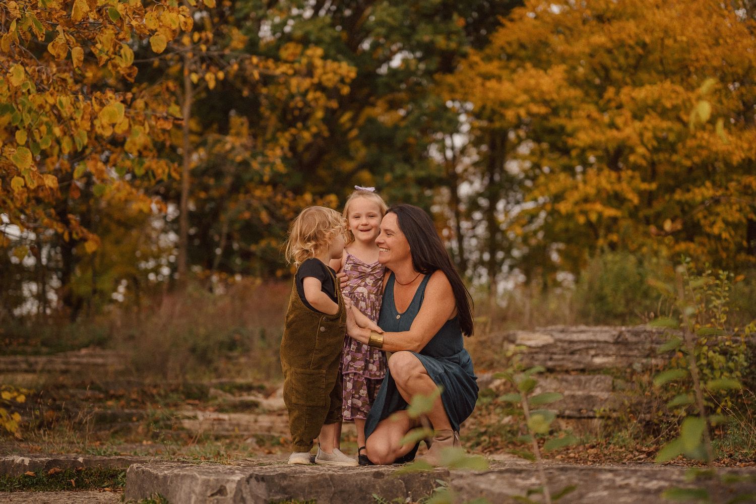 An intimate family moment captured on stone steps surrounded by autumn foliage.