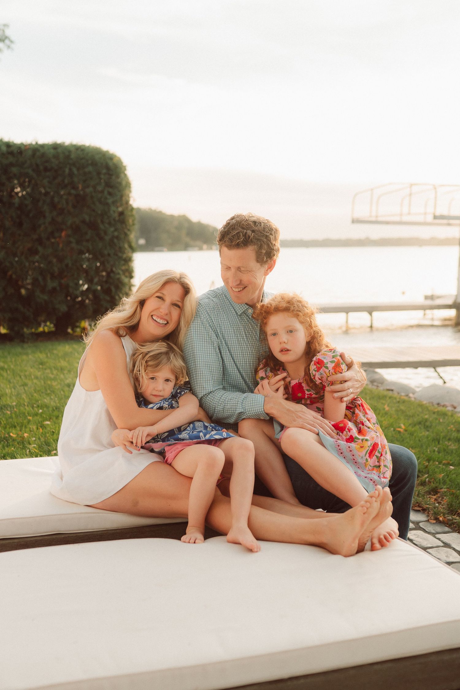 Family relaxing together on a white bench by the waterfront during golden hour.