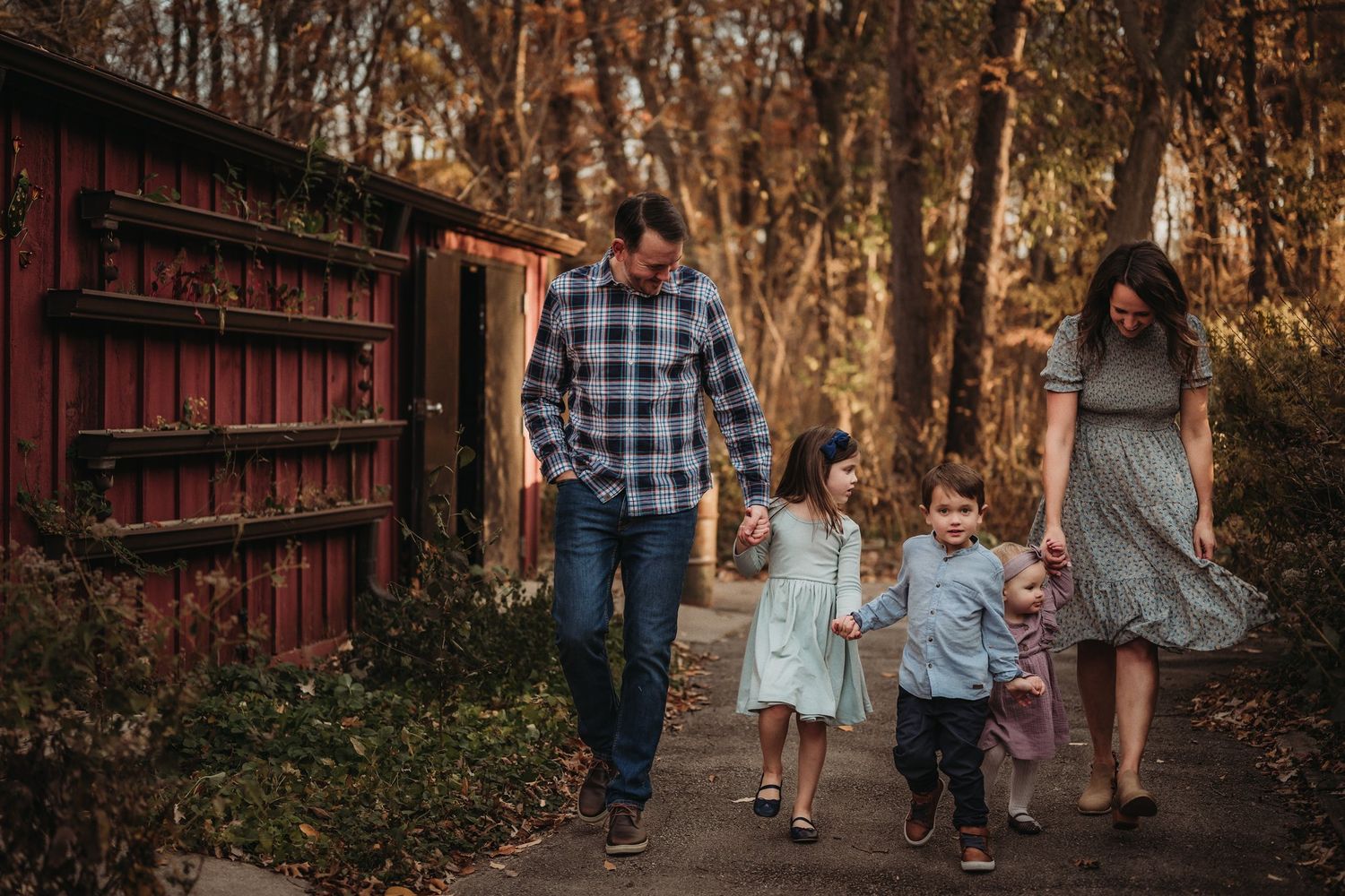 Family strolling together on autumn path beside rustic red barn structure.
