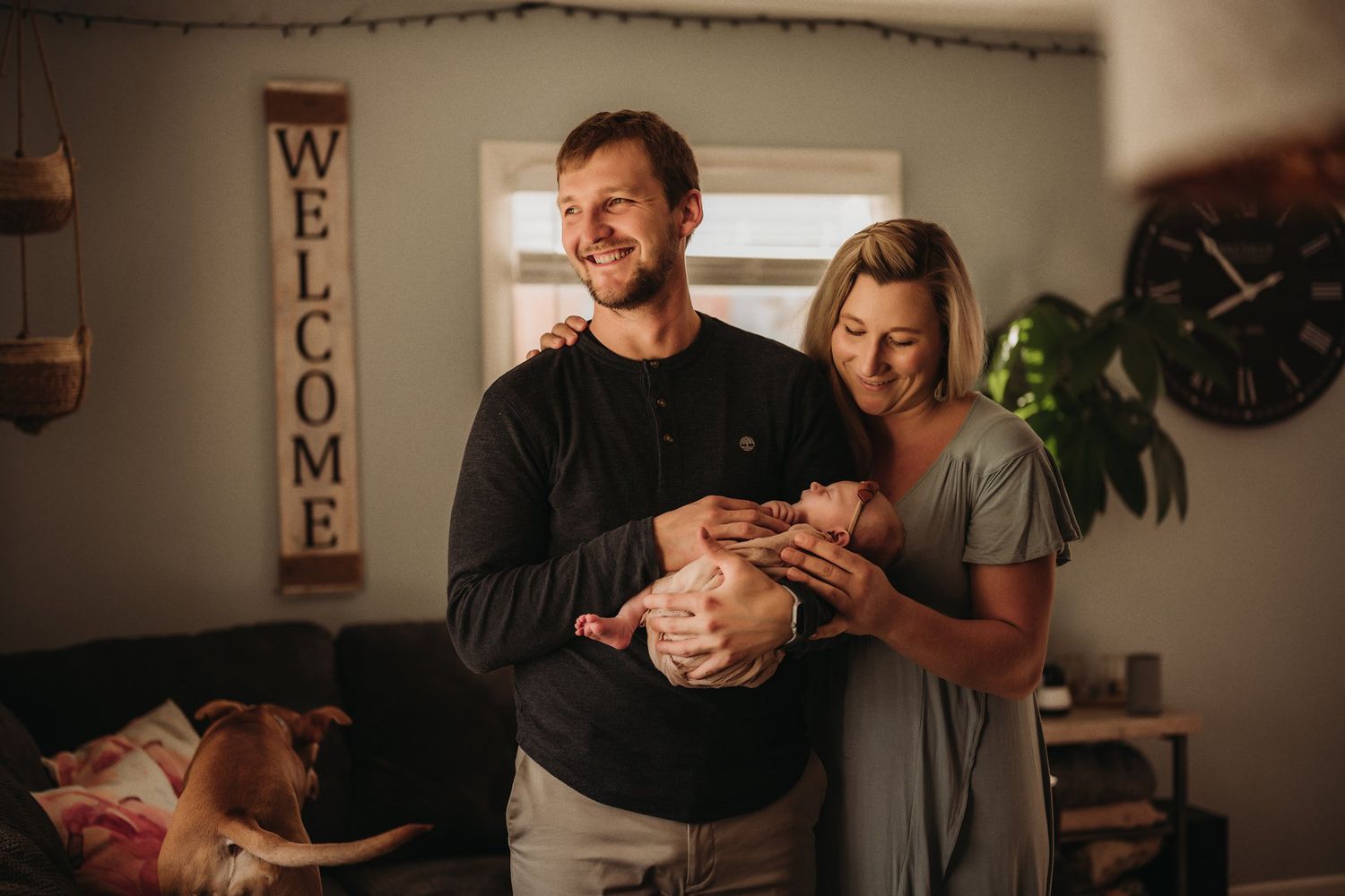 A warm home setting with 'Welcome' sign as adults cradle their newborn by the window.