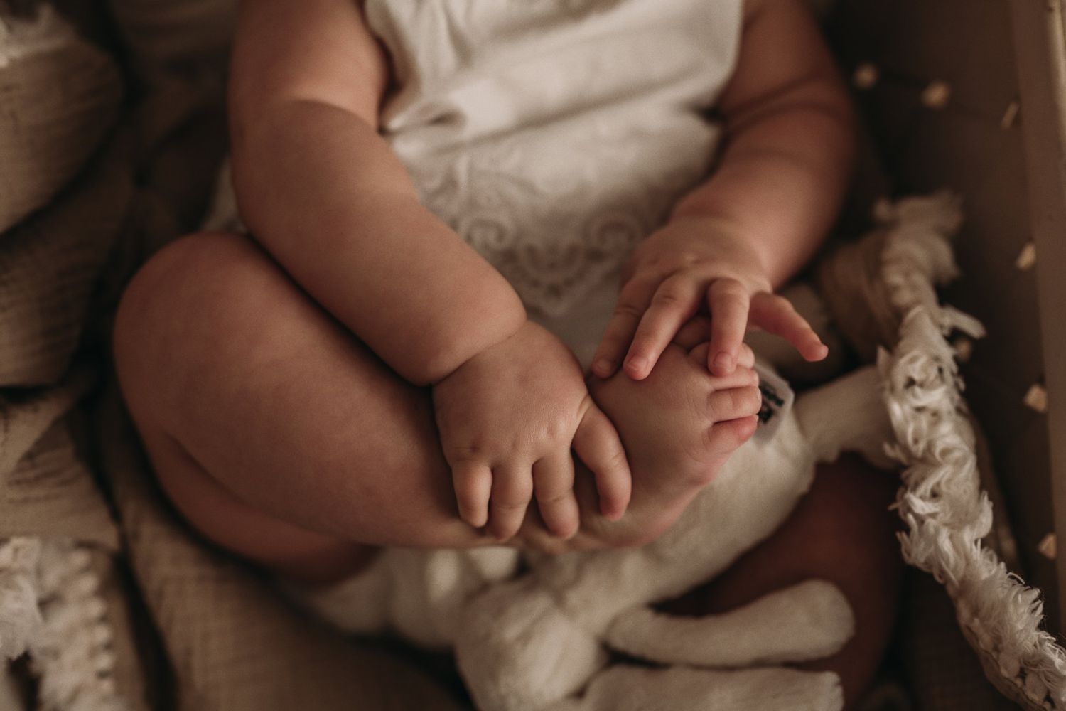 Close-up of baby's hands and feet resting on cream textured fabric.