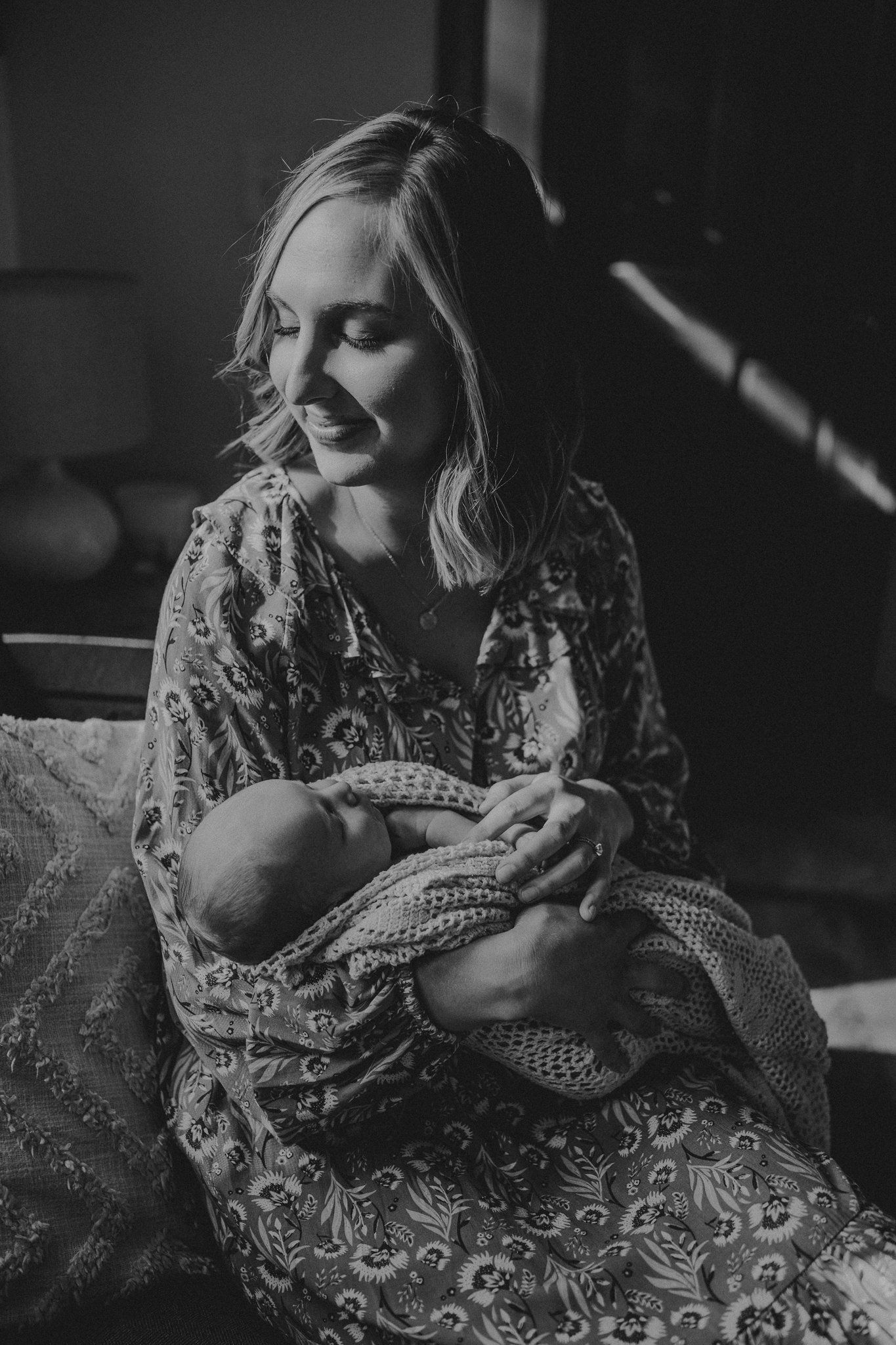 Black and white portrait of mother holding sleeping newborn in knit blanket.