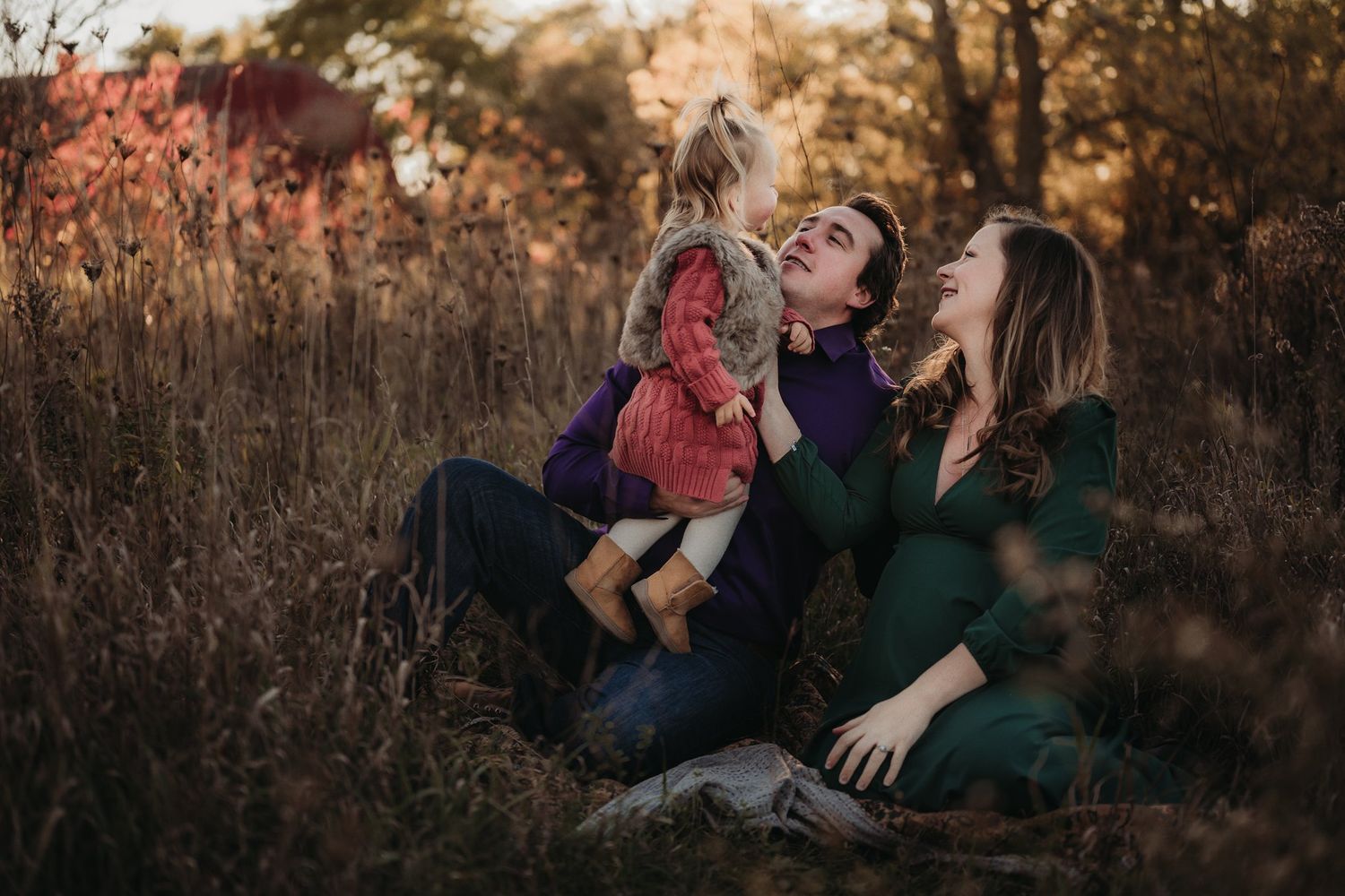 Family sitting together in autumn field during golden hour photography session.