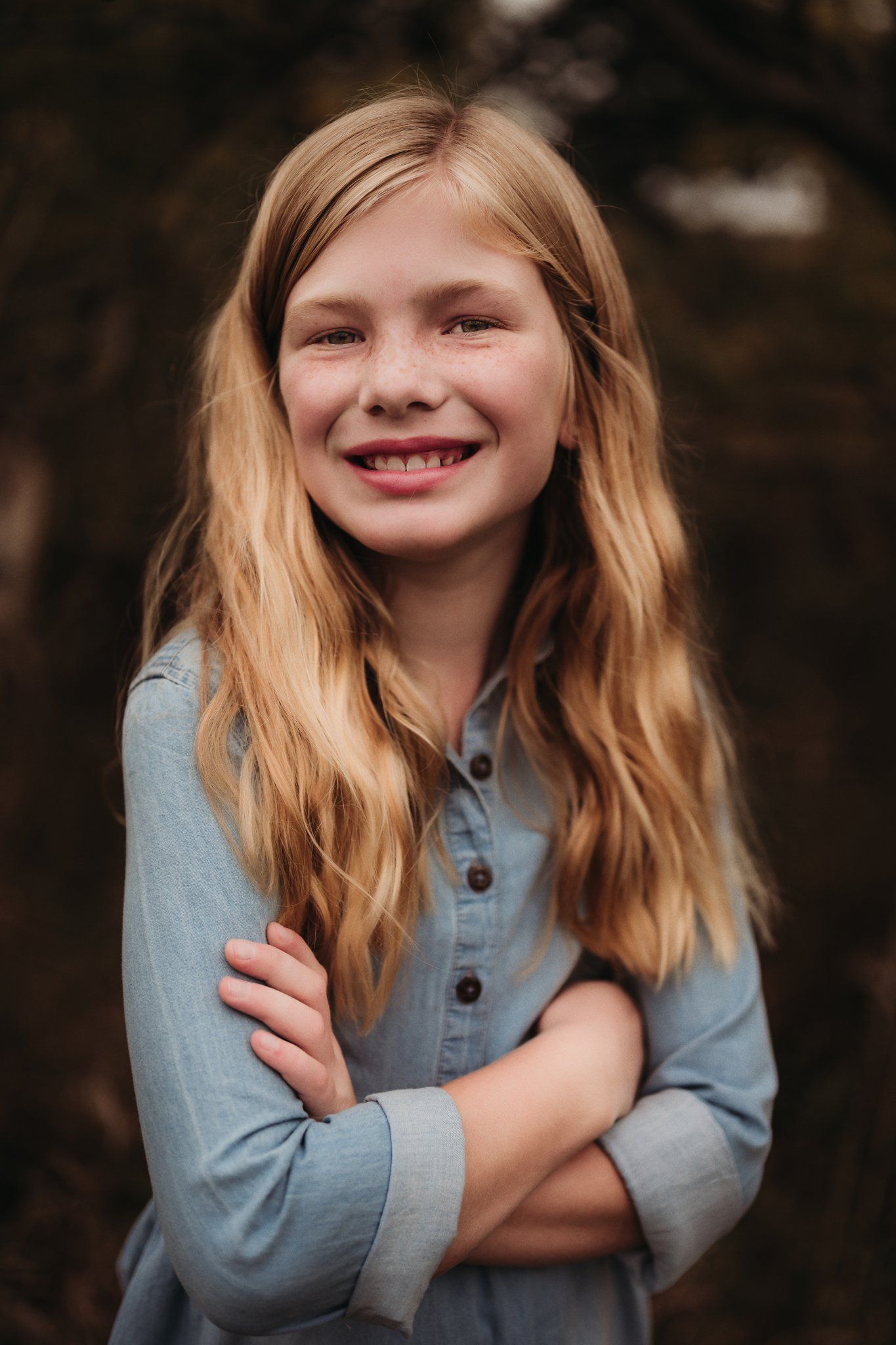 Portrait of person in light blue button-up shirt with long blonde hair smiling against dark background.