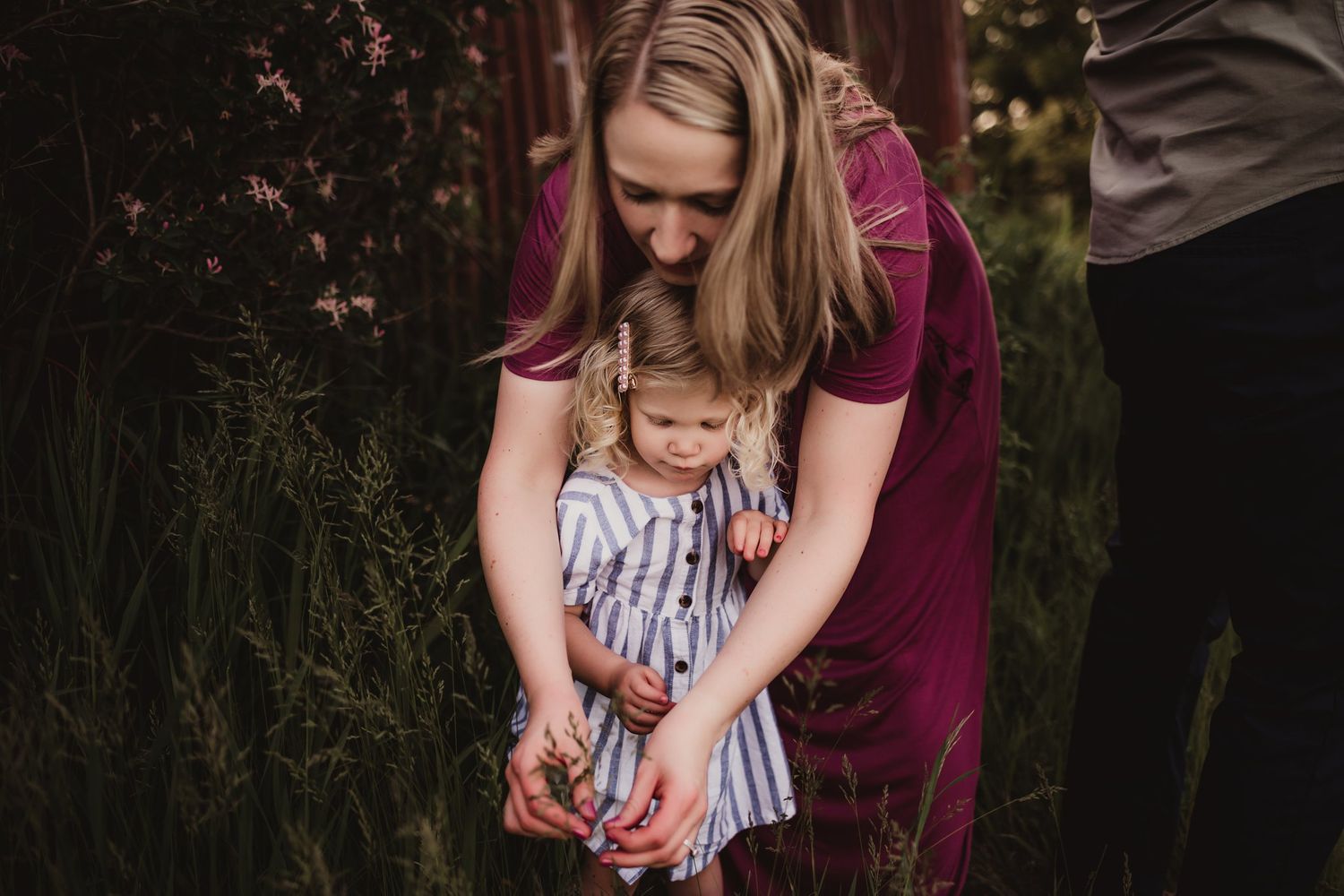 Intimate moment in field shows burgundy-dressed figure embracing striped-dressed child.