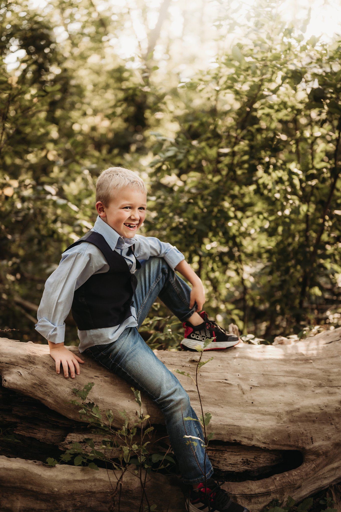 A candid moment captures laughter while sitting on a fallen log in dappled sunlight.