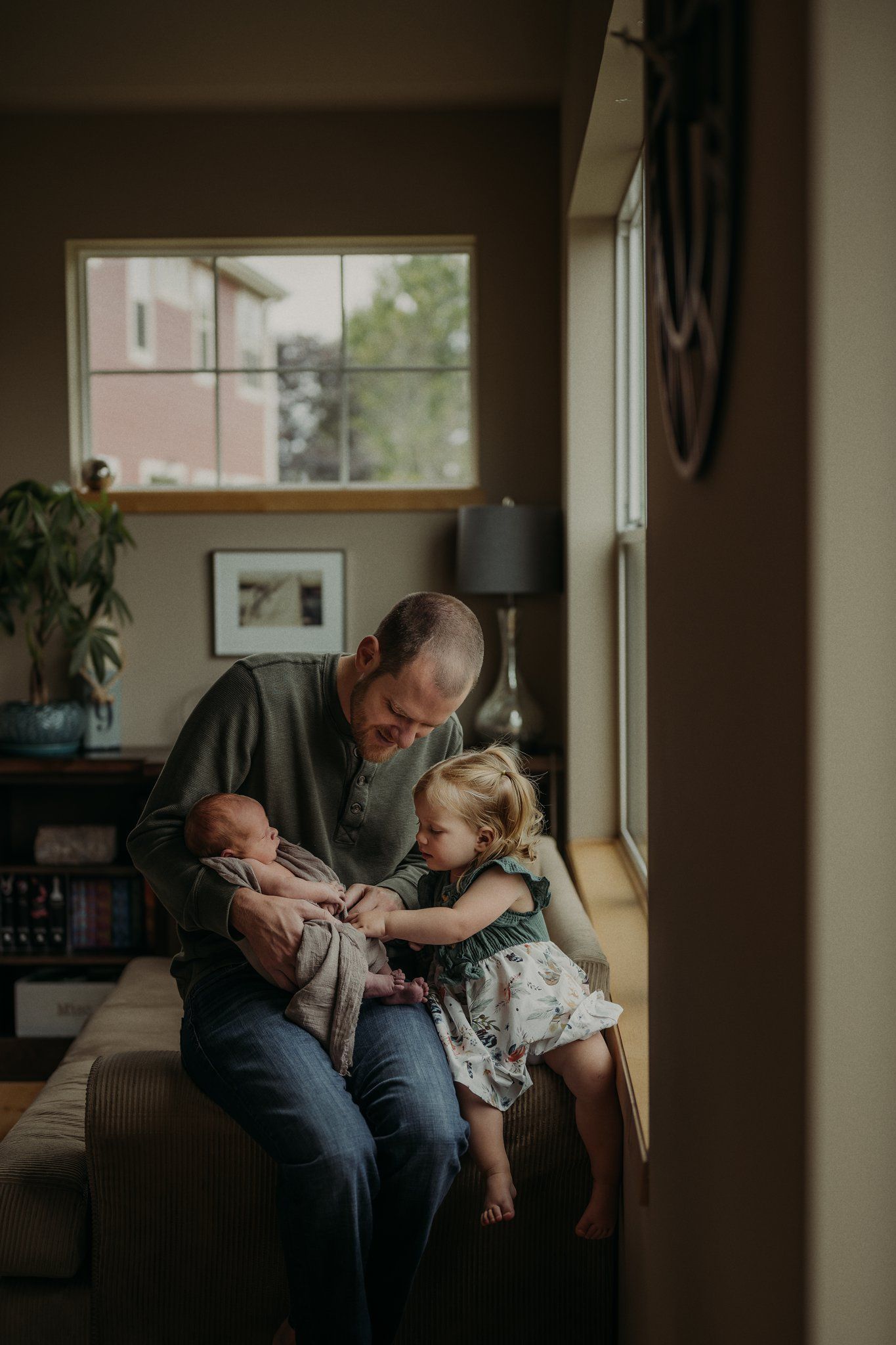Intimate family scene with siblings and parent by window with houseplant in background.