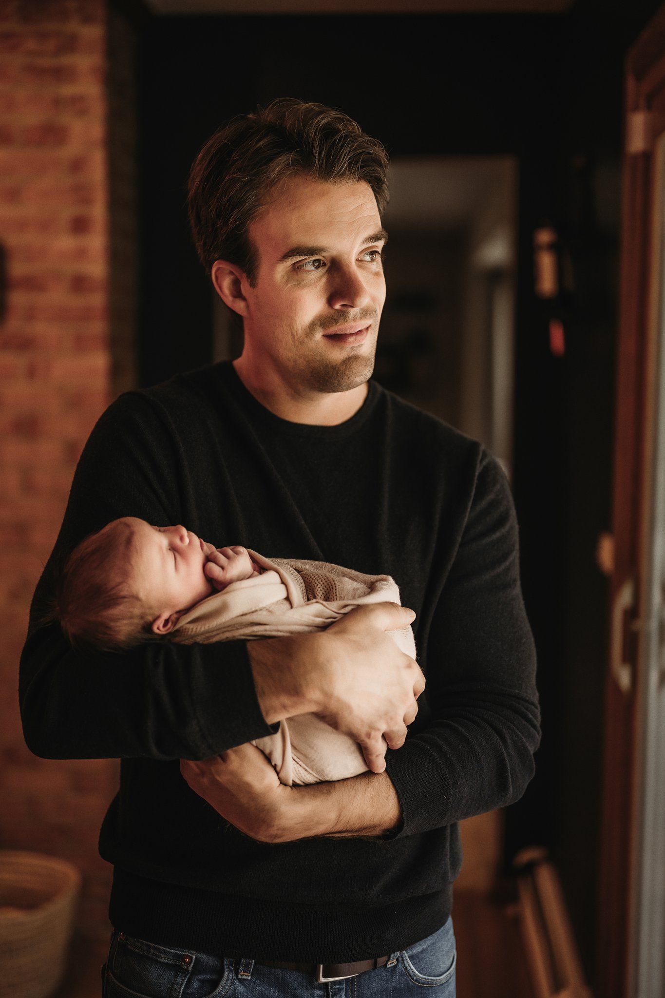 Indoor portrait with newborn against rustic brick wall background.