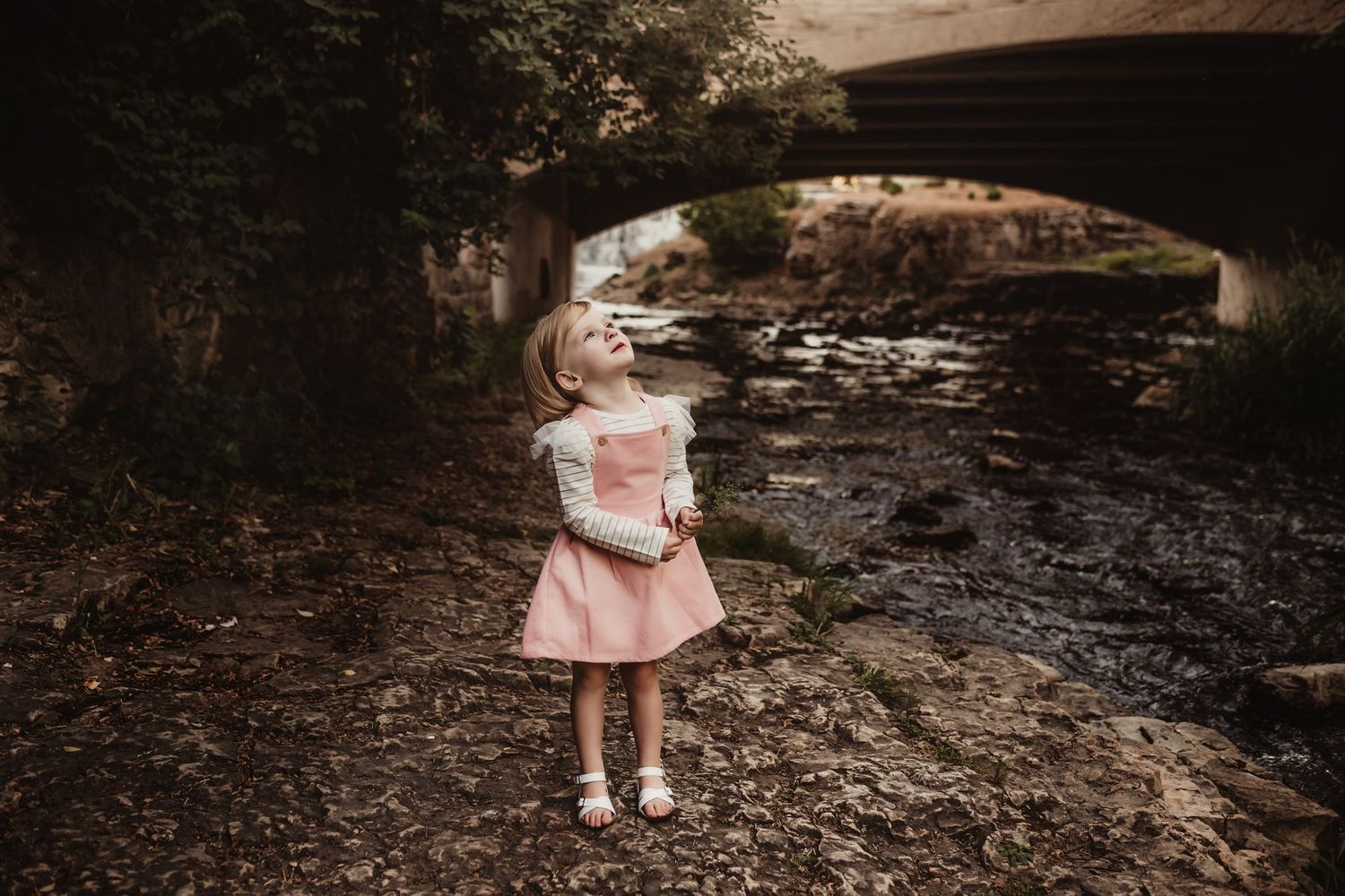 A pink dress outfit photographed under a stone bridge by a stream.