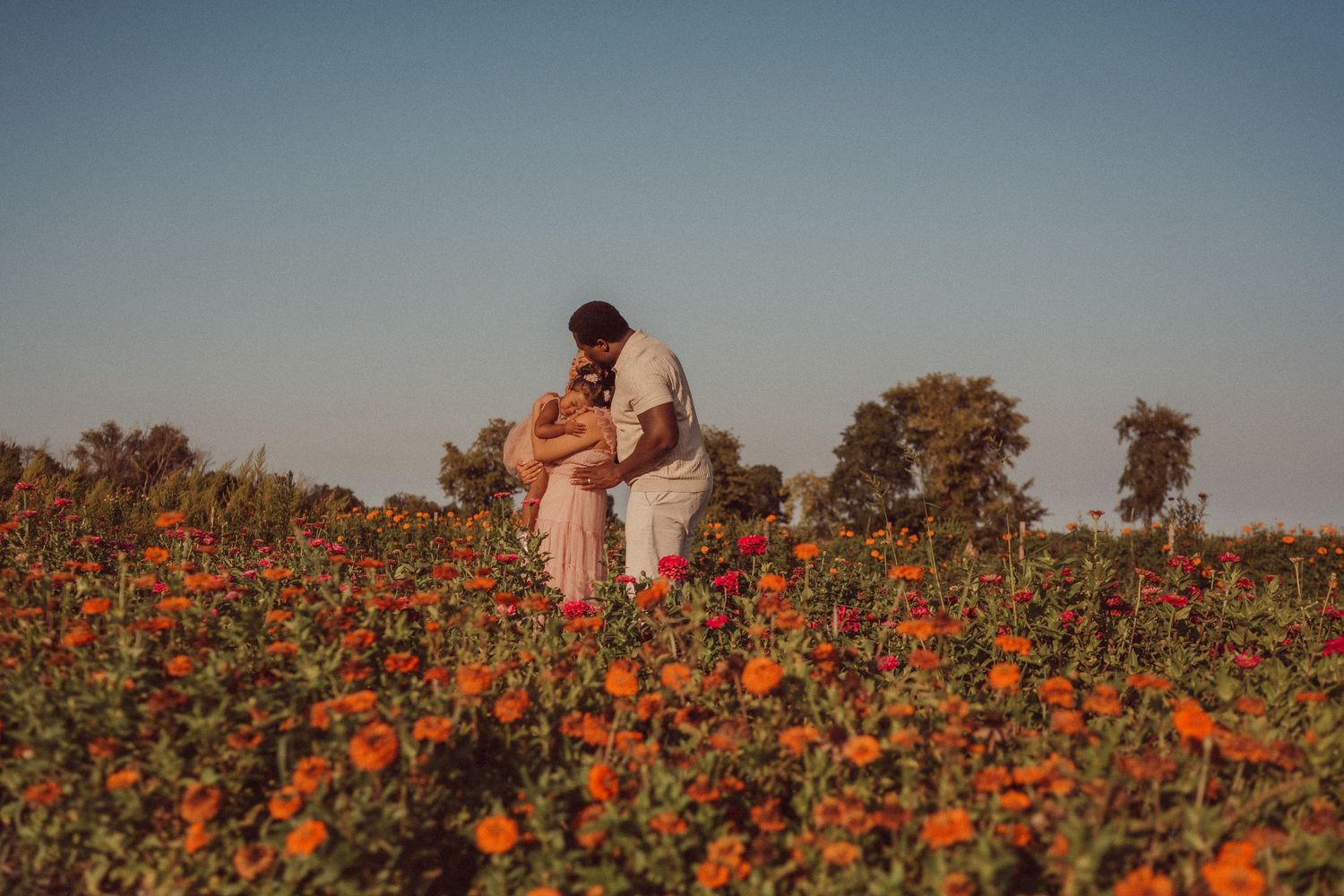 Couple sharing an intimate moment surrounded by orange wildflowers at sunset.