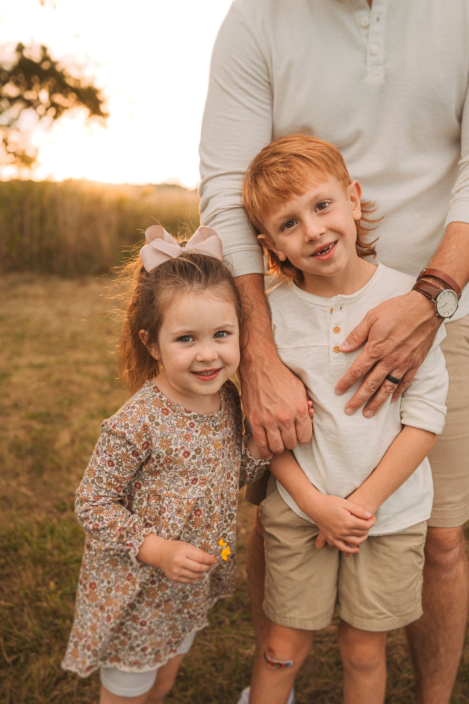 Children and adult standing together outdoors at sunset in casual clothing.
