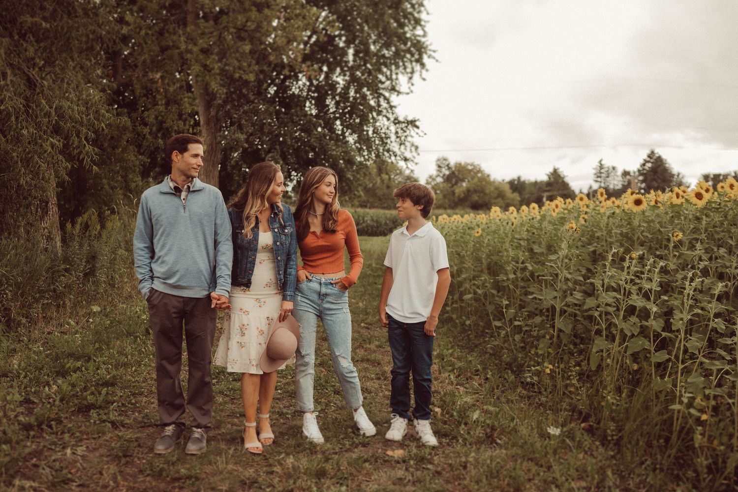 A group poses together on a rustic path beside a sunflower field.