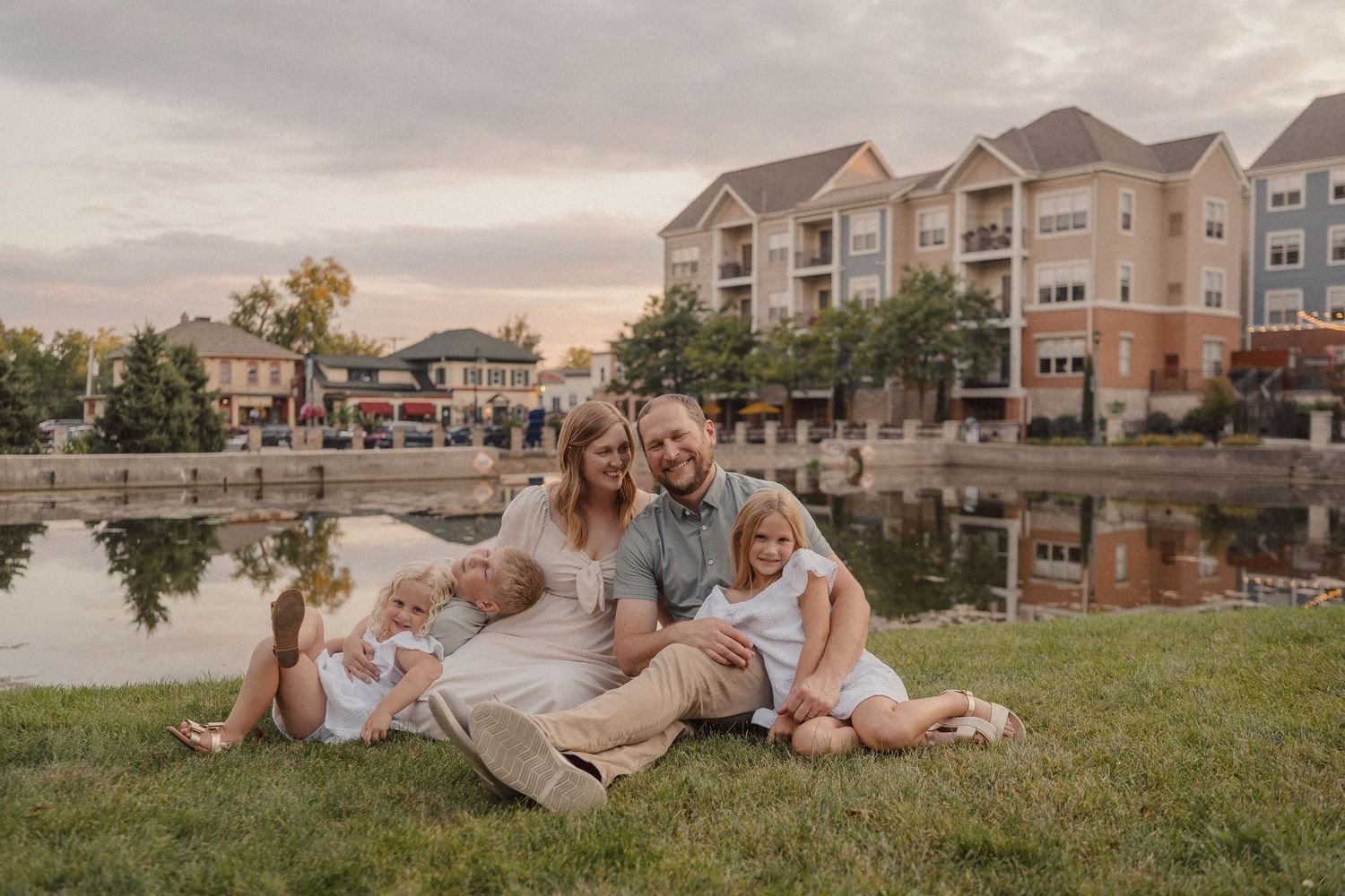 Family enjoying a sunset photo session in a grassy area with apartment buildings in the background.