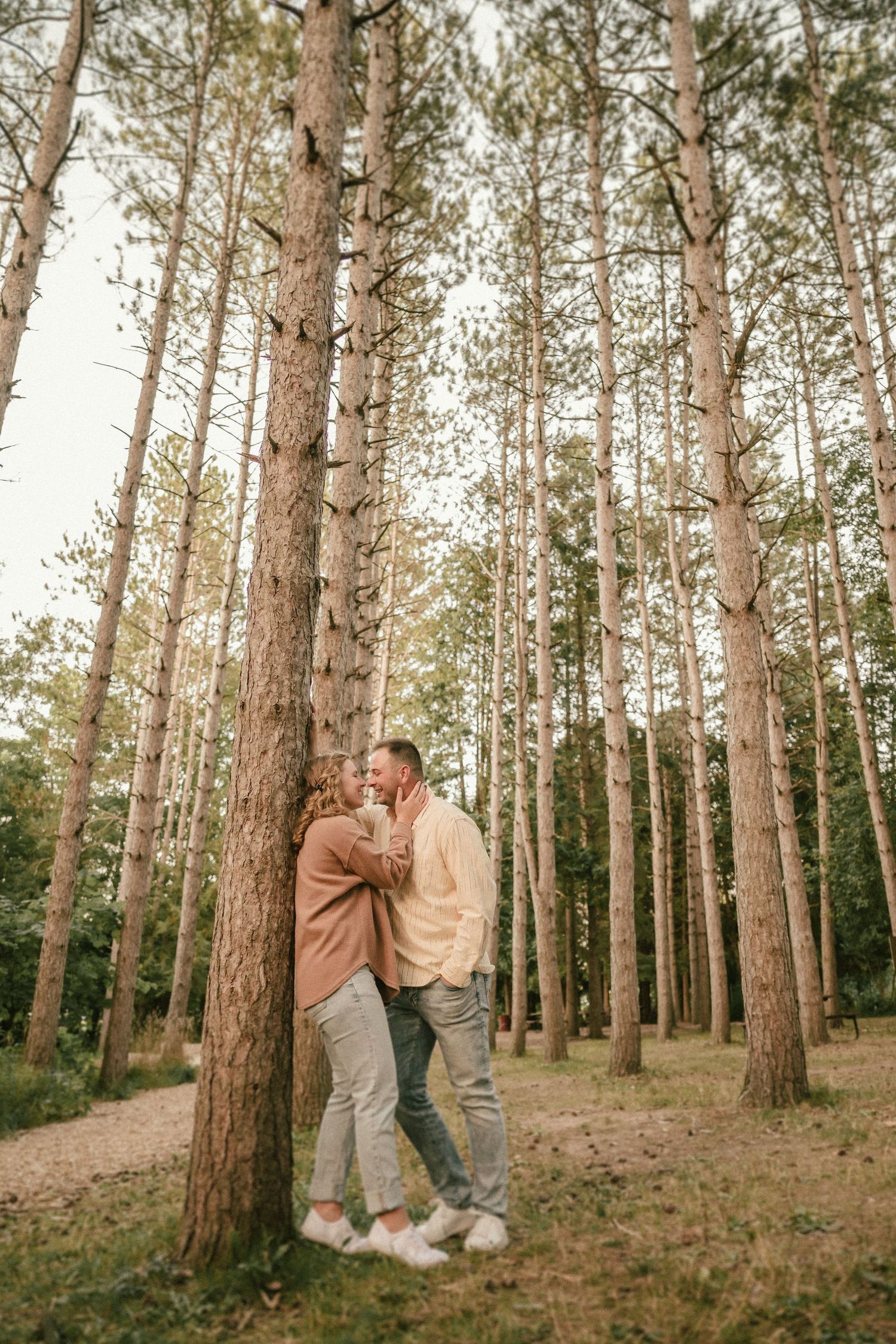 Couple shares romantic moment among tall pine trees in forest setting.
