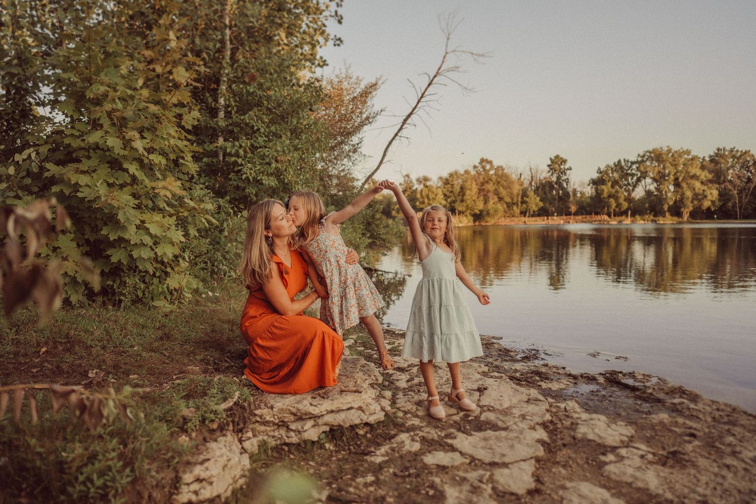 A group sitting by a serene lake during golden hour surrounded by autumn foliage.