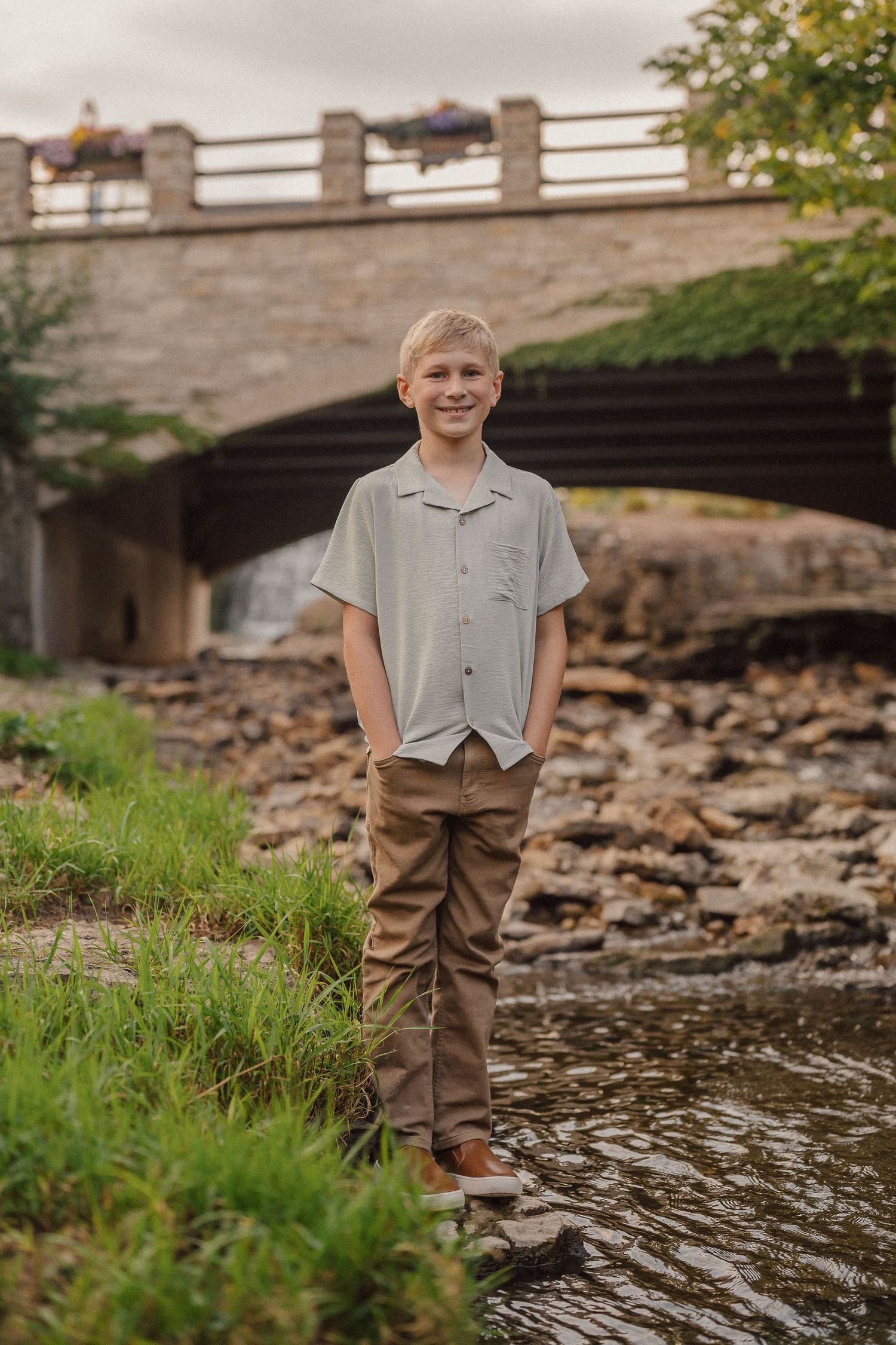 Child standing near a stone bridge over a rocky creek bed with water flowing beneath.
