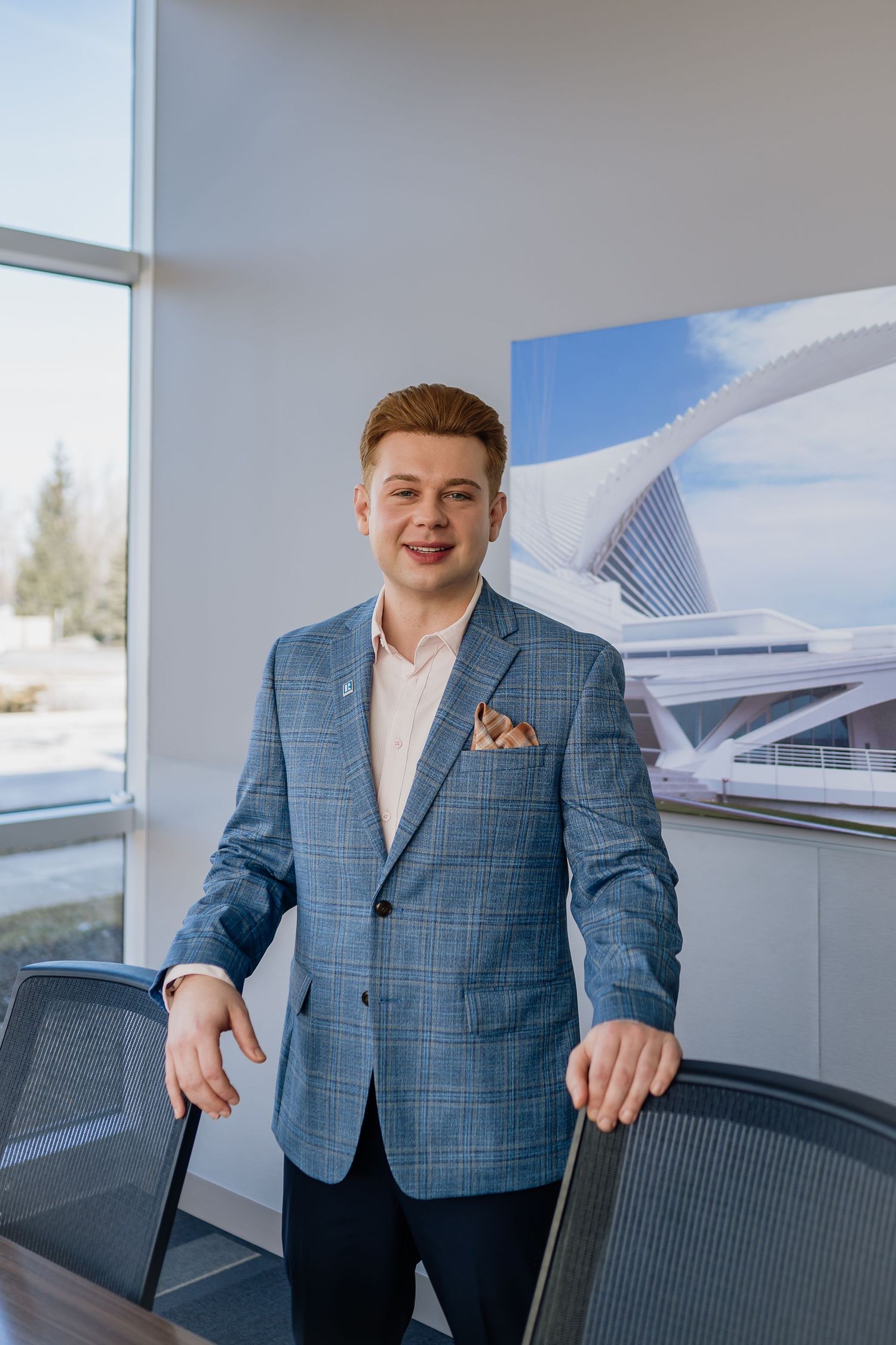 Professional portrait in modern office setting with architectural artwork and blue plaid blazer.