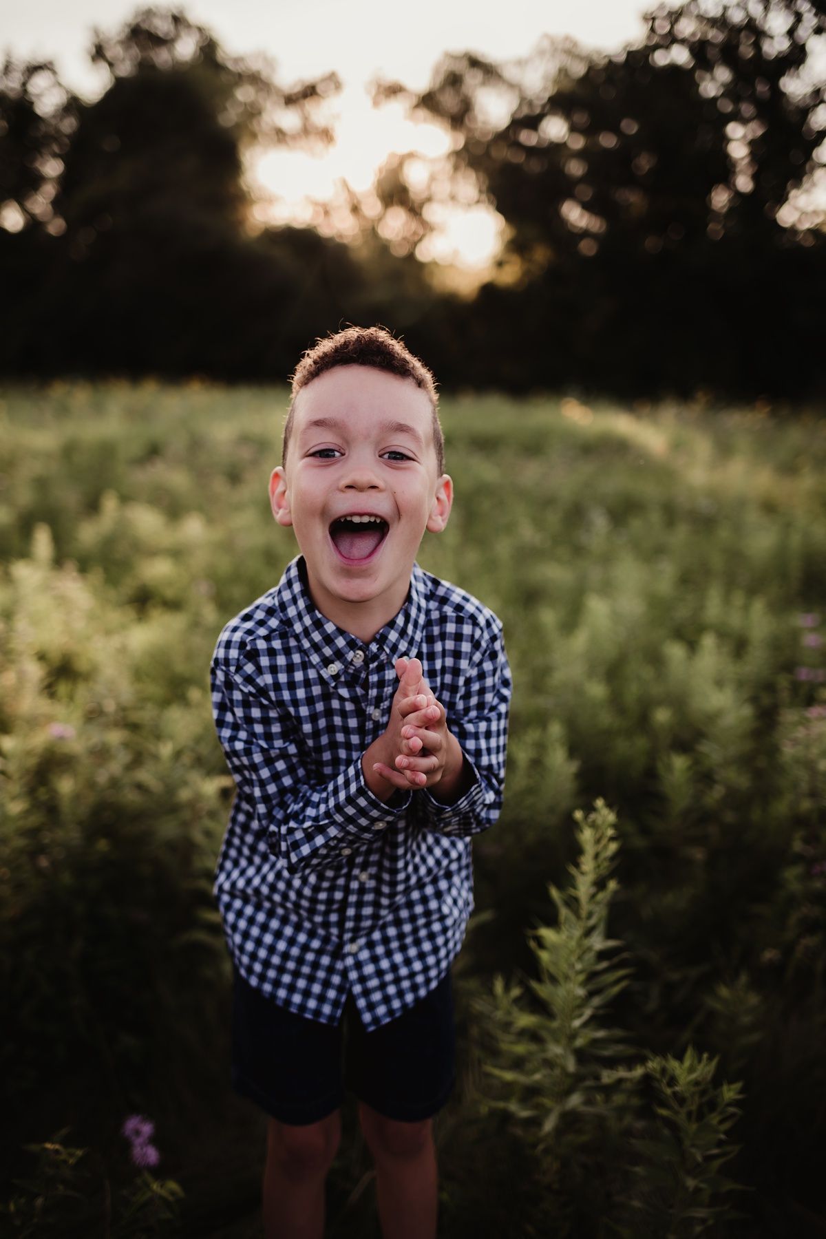 Child in blue checkered shirt expressing pure joy while playing in a meadow at sunset.