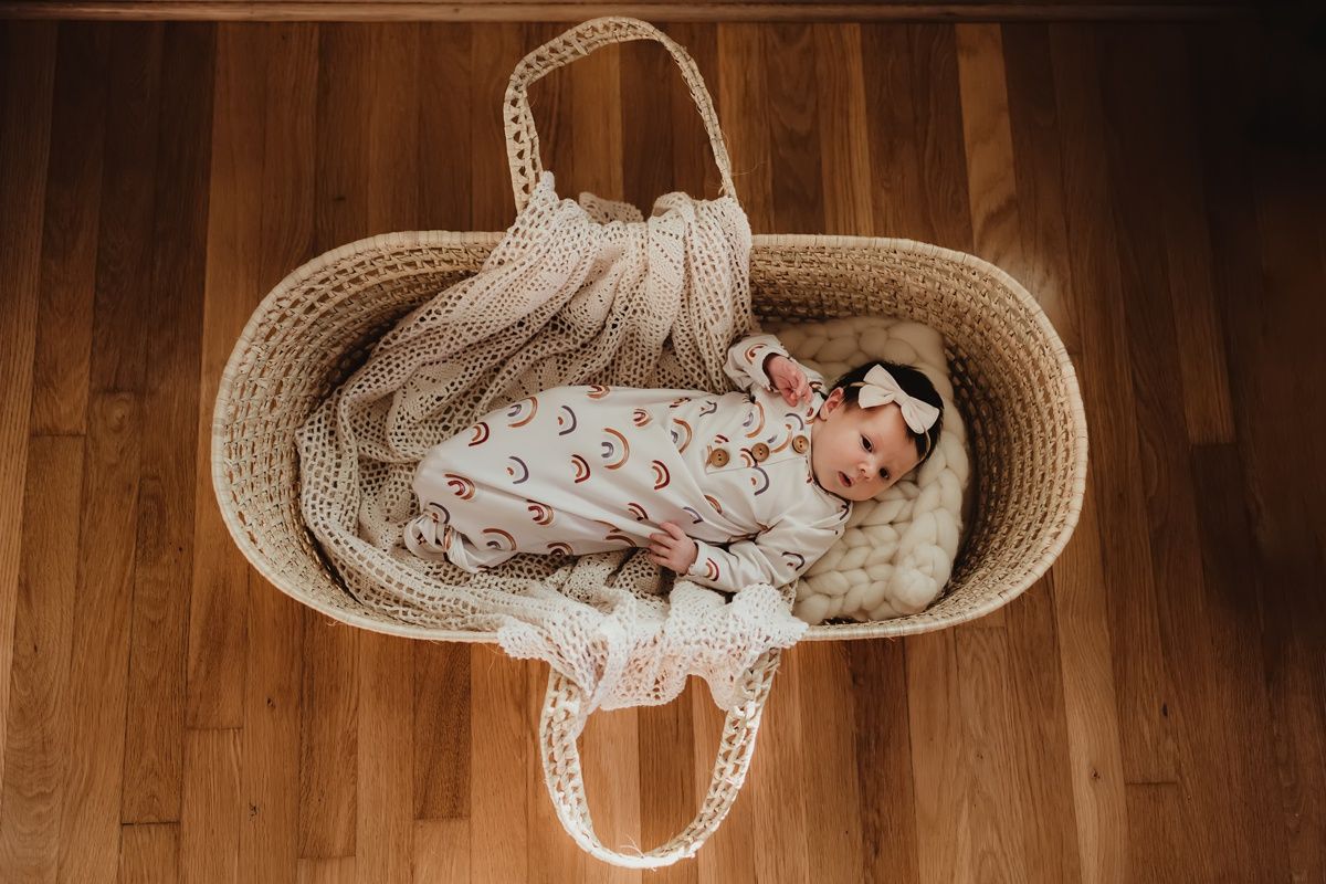 Overhead view of infant resting in woven moses basket on hardwood floor.