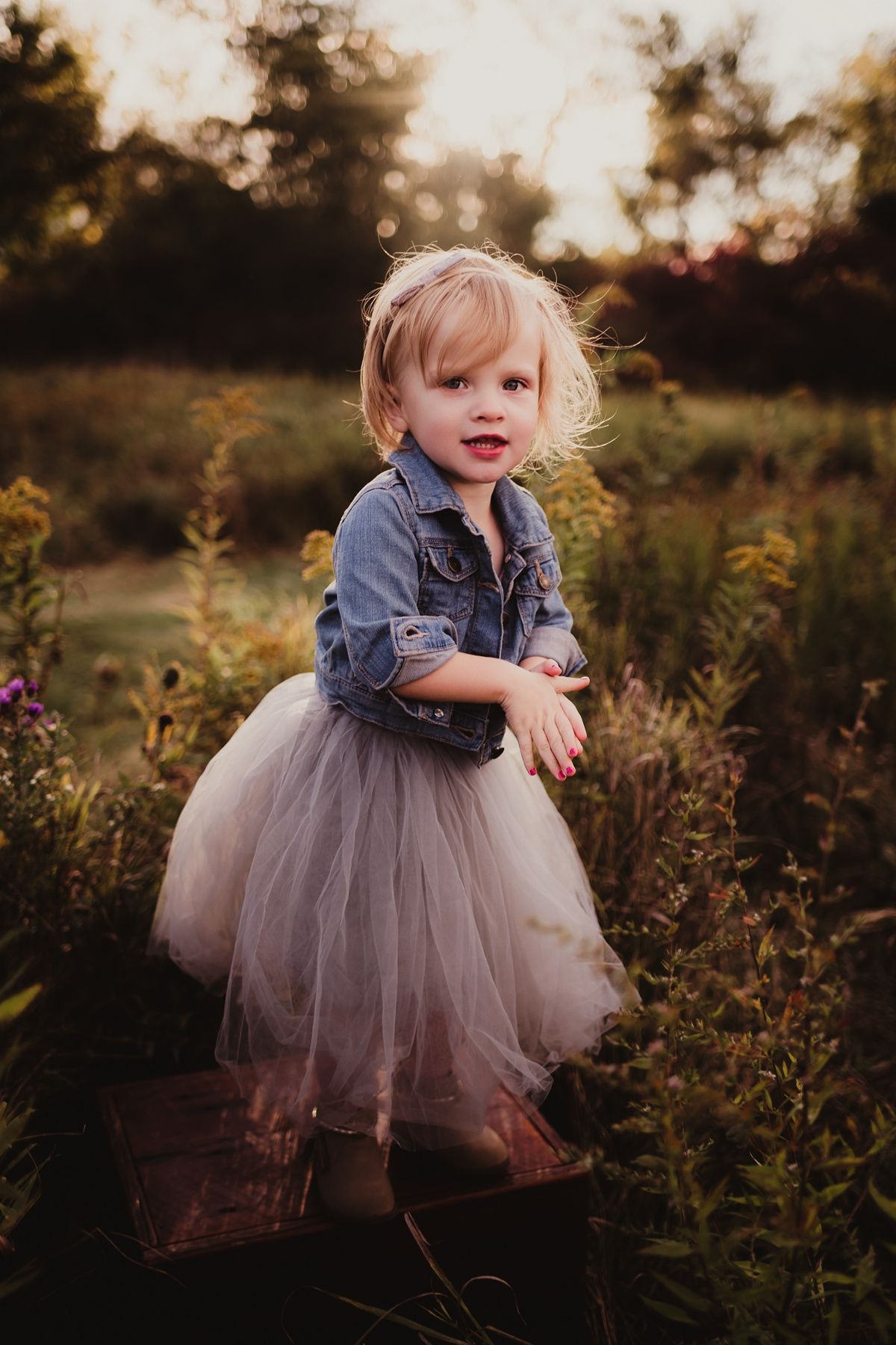 Sunset portrait showing playful pose on wooden platform surrounded by wildflowers.
