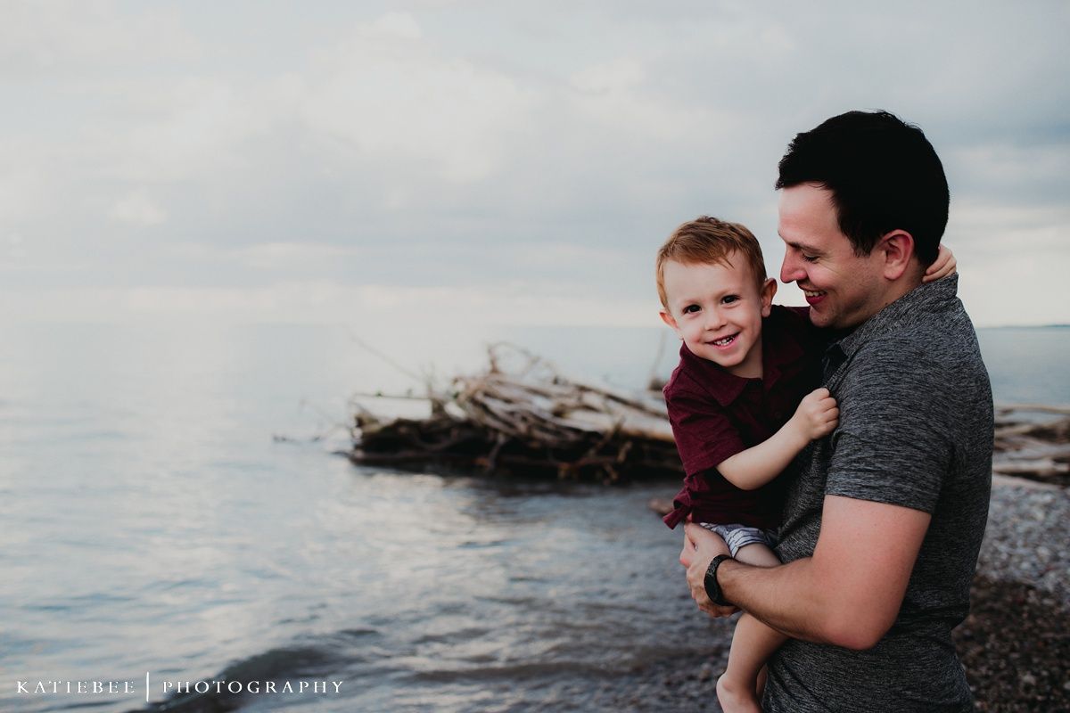 Candid moment shared between parent and child on rocky beach with ocean view.