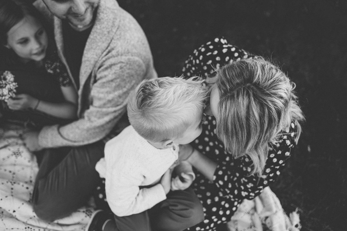 Black and white candid photo of a family sharing a playful moment together outdoors.